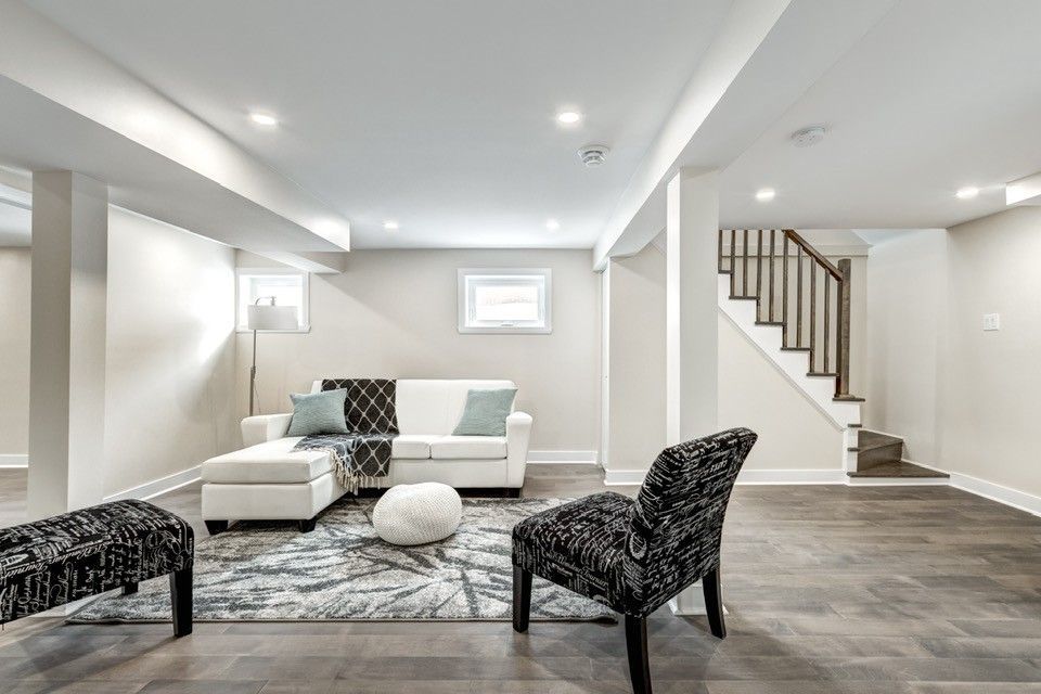 Finished basement living space with a white sectional sofa, patterned rug, and stairs.