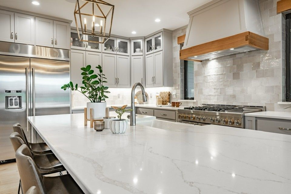 Modern kitchen with large white countertop island, stainless steel appliances, grey cabinets, and pendant lighting.