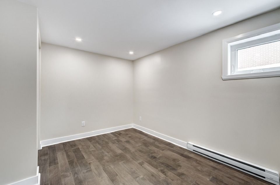 Empty room with wood-look flooring, white walls, recessed lighting, small window, and baseboard heater.