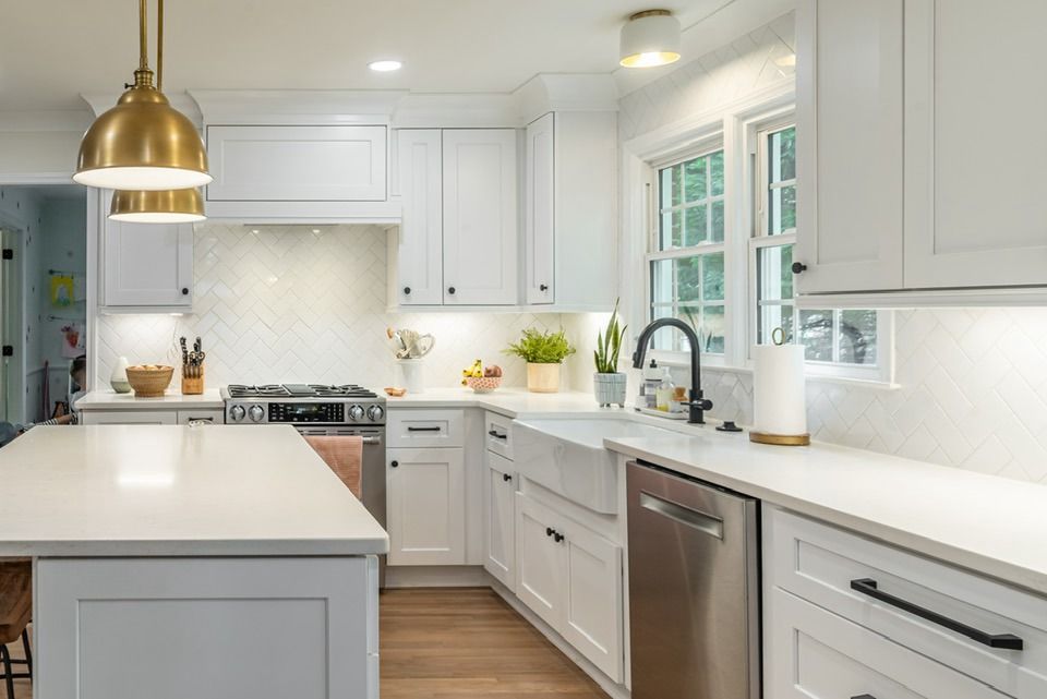 White kitchen with island, stainless steel appliances, and gold pendant lights.