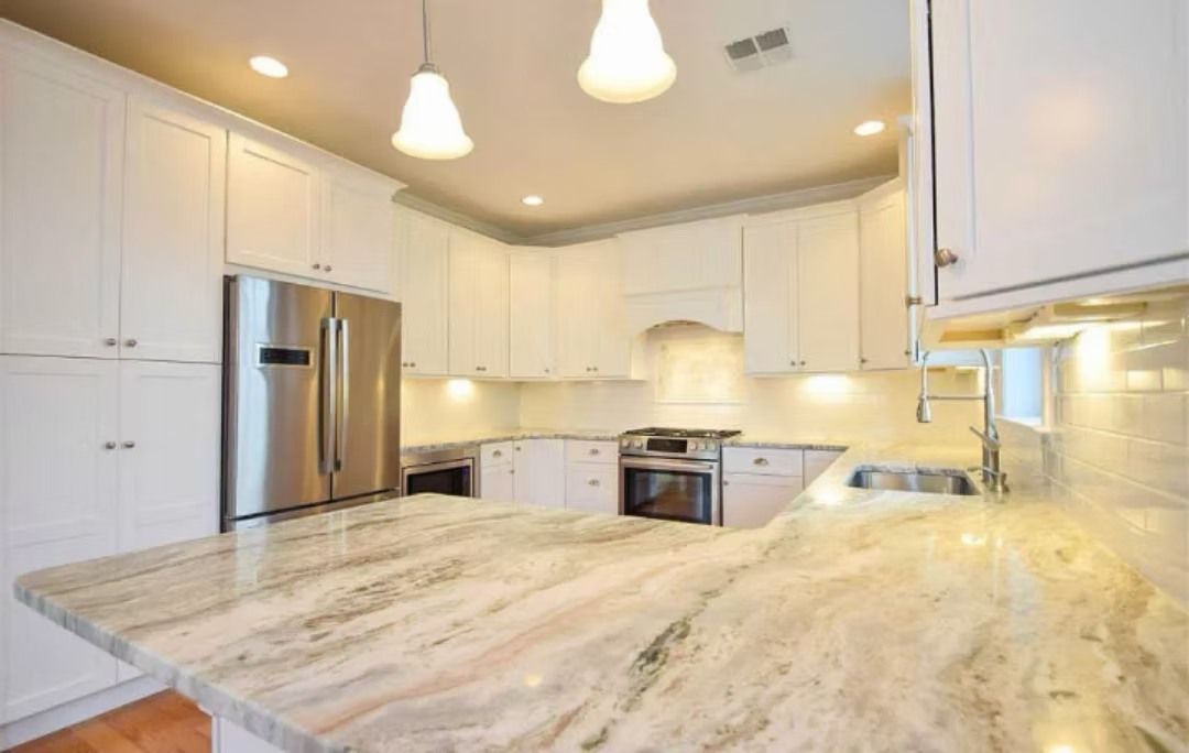 A white kitchen with granite countertops, stainless steel appliances, and overhead lighting.