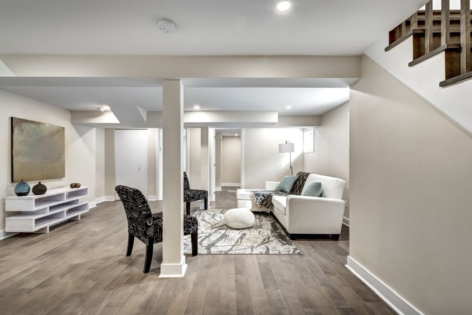 Finished basement living room with a white couch, chairs, and wood-look flooring.