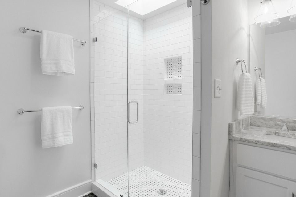 White-tiled shower with glass door and white towels on the wall. Bright, modern bathroom.