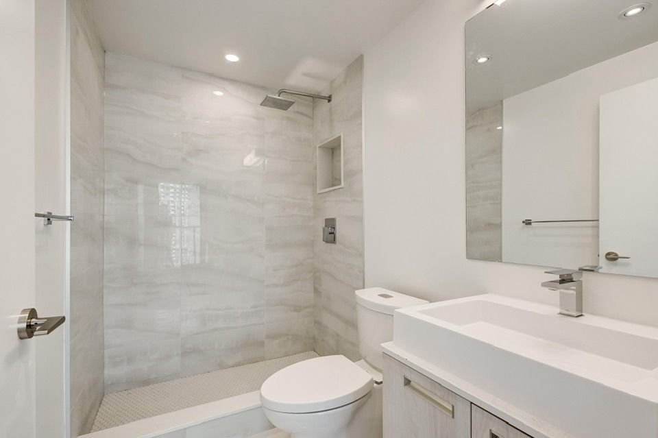 Modern bathroom with white marble shower, toilet, and sink.