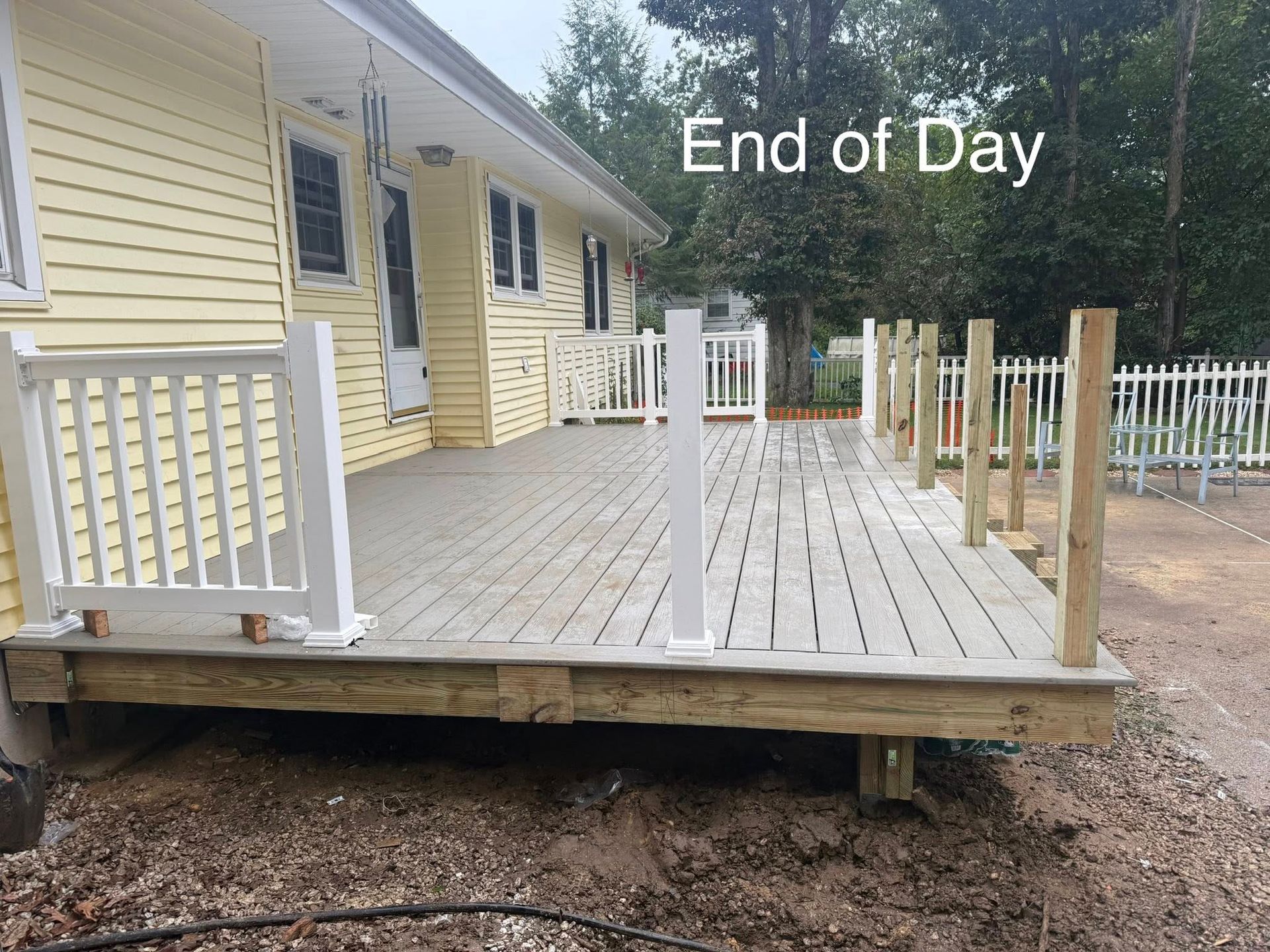 Partially built deck on a yellow house.  White railings, gray deck boards, and wooden posts visible.