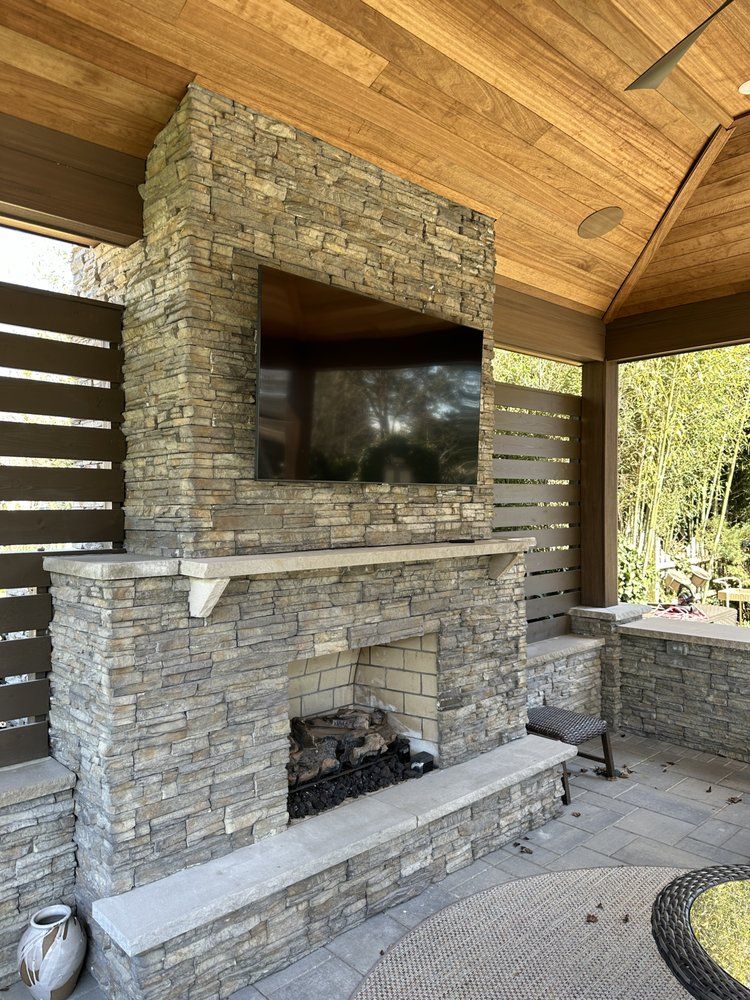 Outdoor fireplace with mounted TV, stone facade, and wooden ceiling.