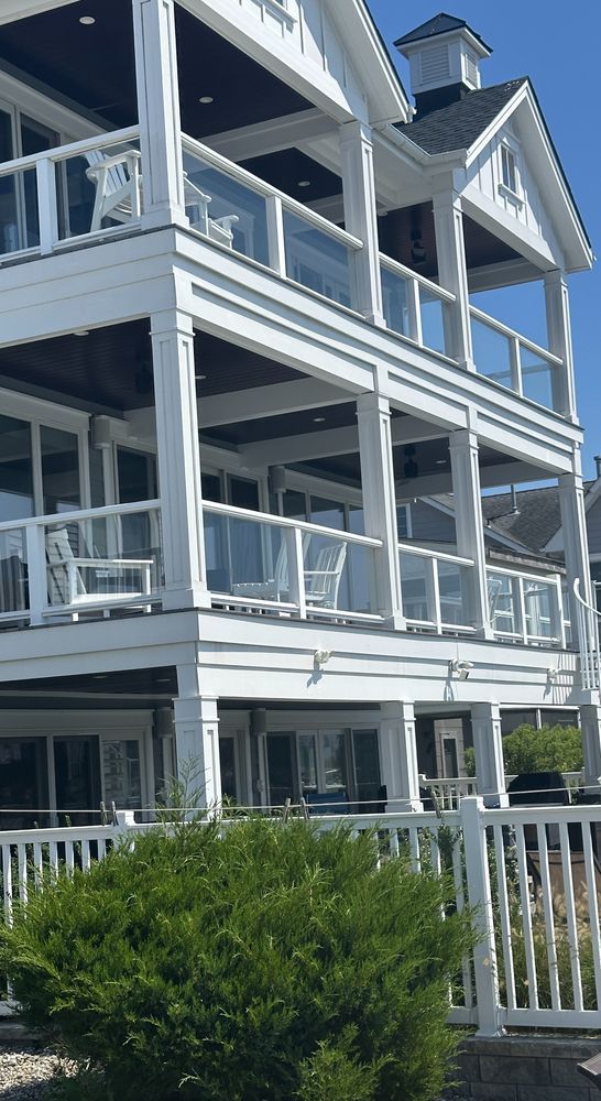 White multi-story house with glass balconies, topped with a small tower, and white picket fence.