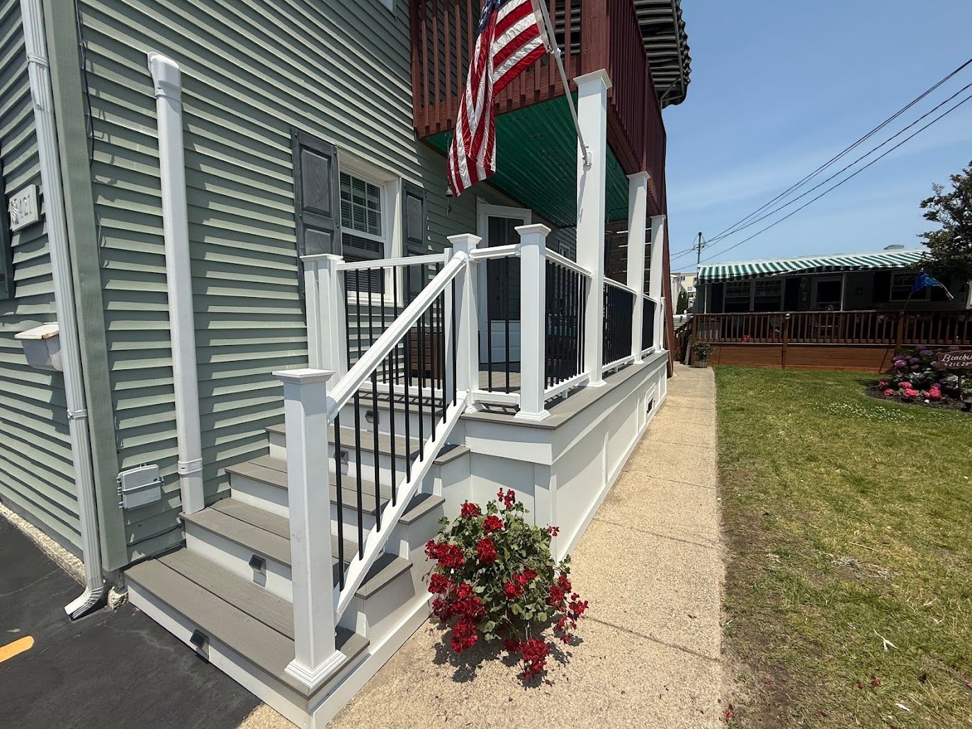 A house with a porch and steps, white railing and American flag. Red roses in front.