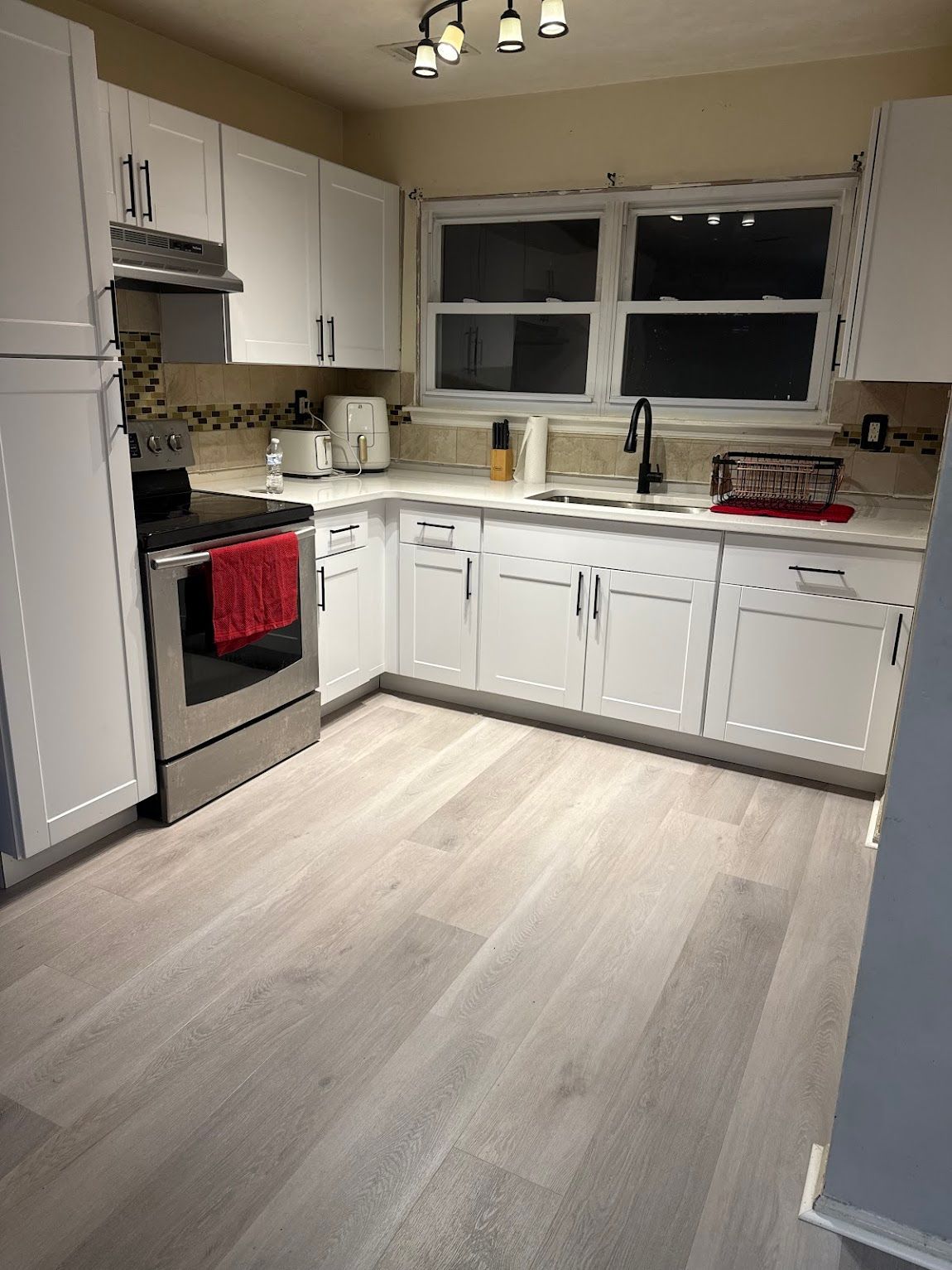 White kitchen with stainless steel appliances, white cabinets, and light gray wood-look flooring.