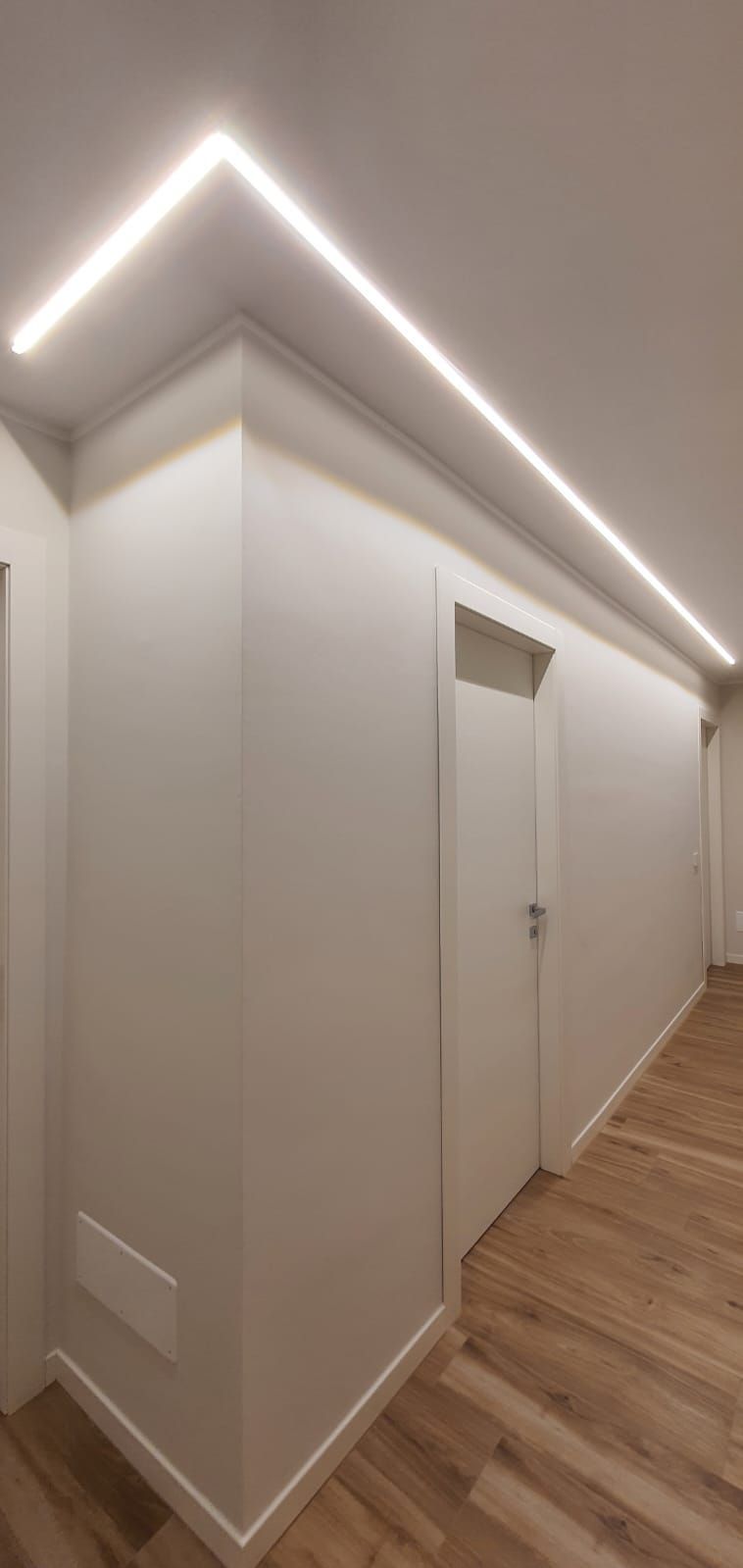 Un lungo corridoio con pavimento in legno e pareti bianche.