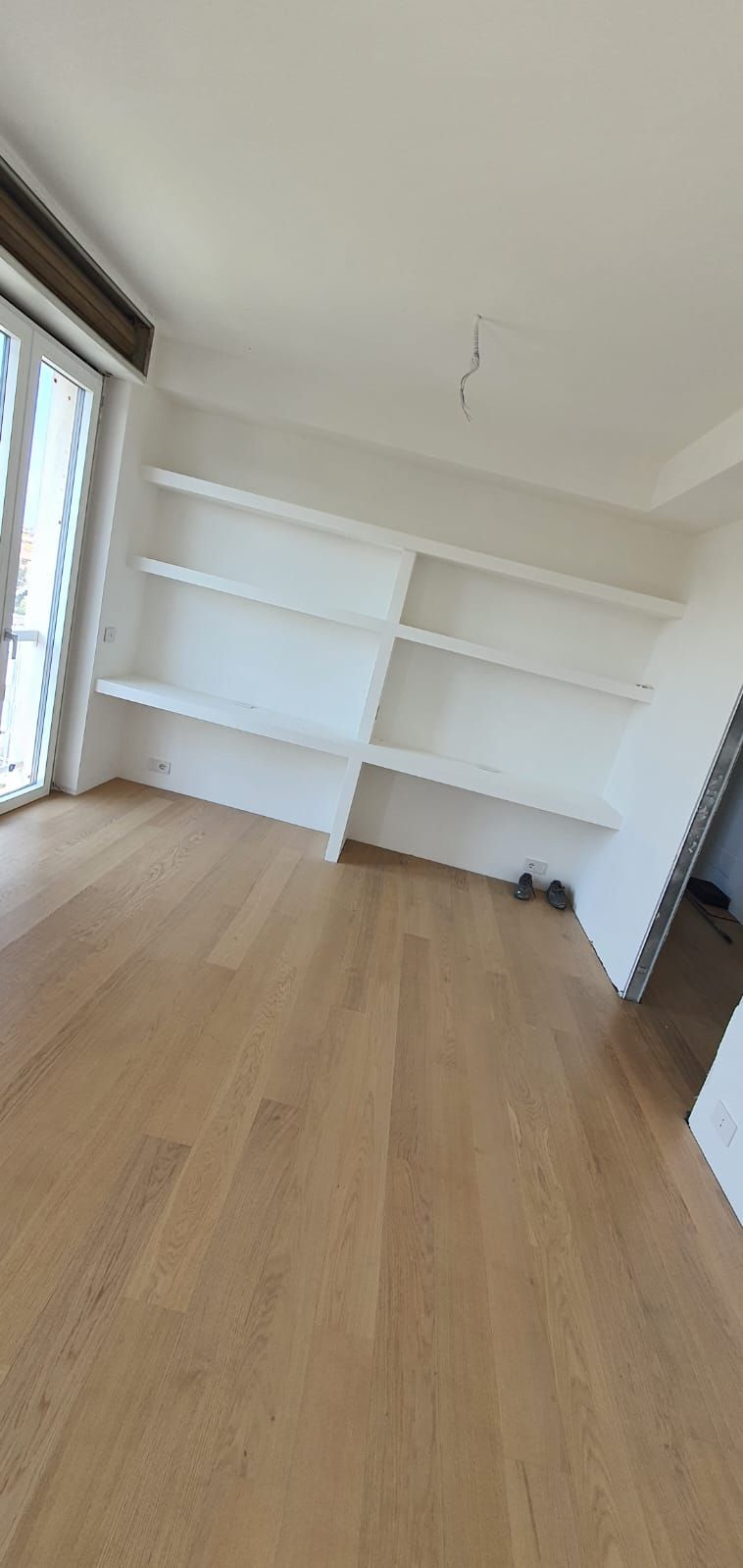 Un soggiorno con pavimenti in legno e scaffali bianchi.