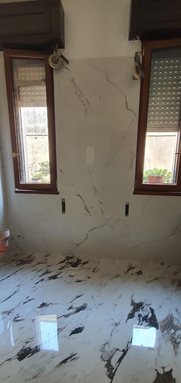 Una stanza con pavimento in marmo e due finestre.