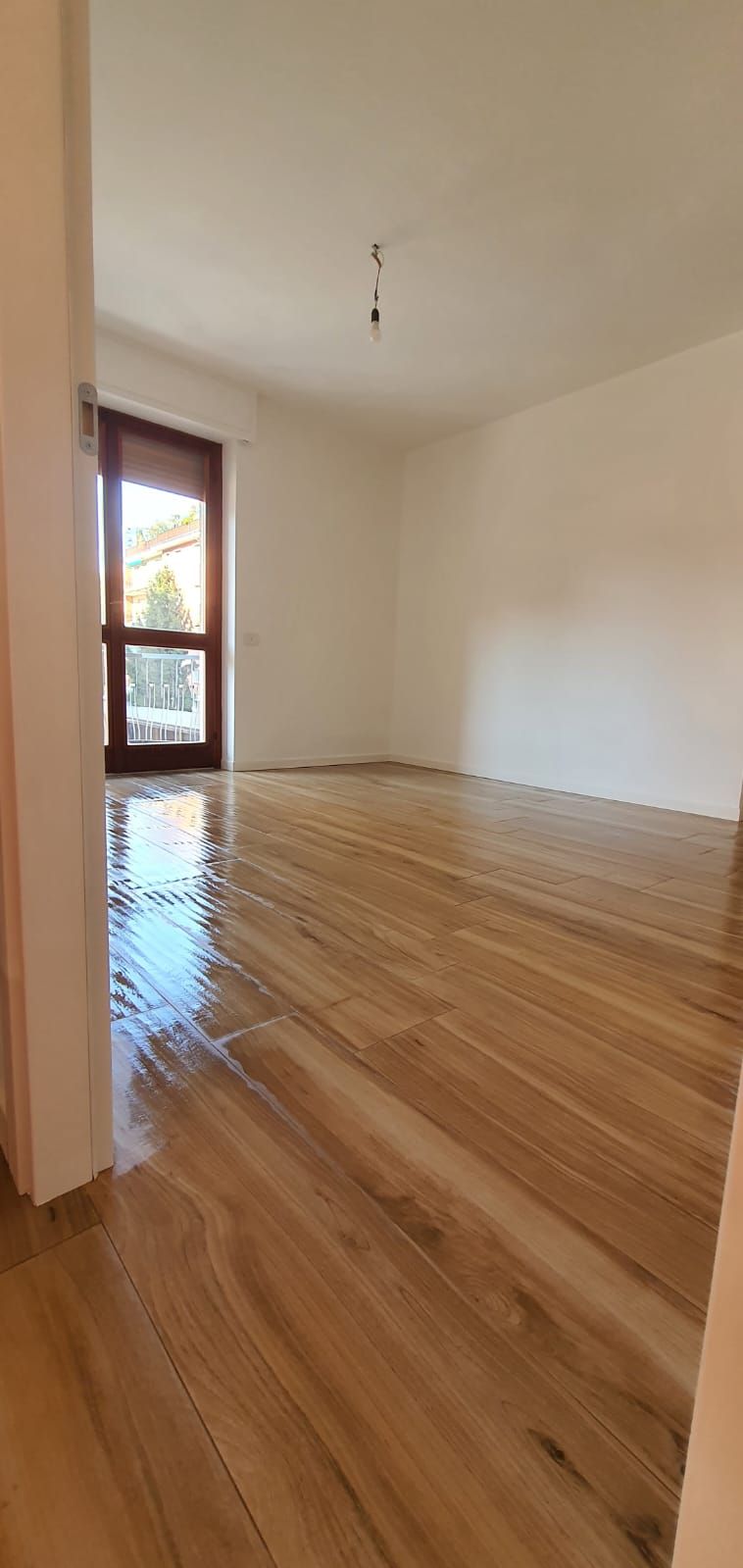 Una stanza vuota con pavimento in legno e una porta scorrevole in vetro.