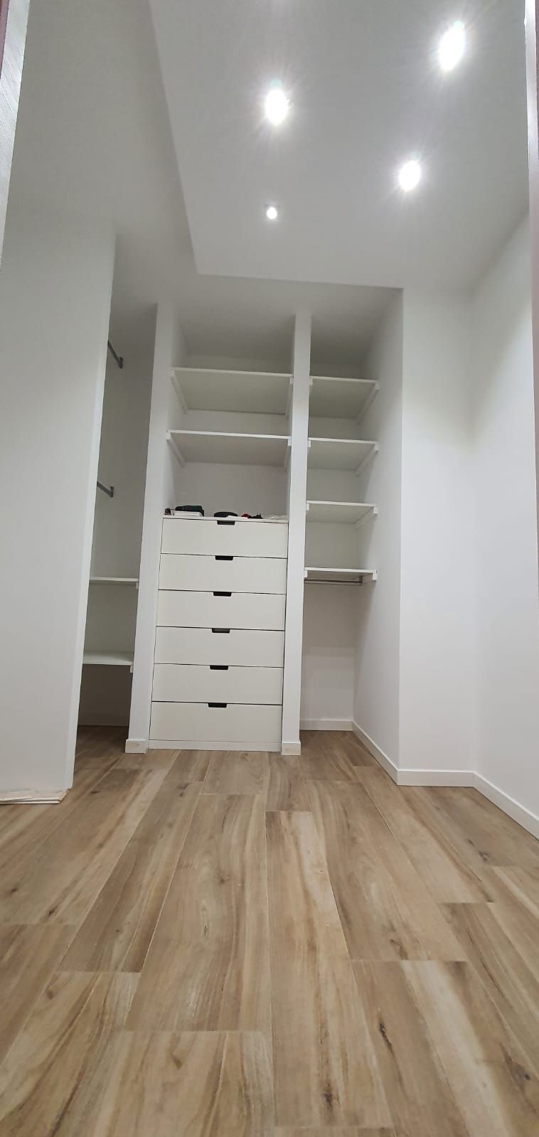 Una cabina armadio con pavimenti in legno e ripiani bianchi.