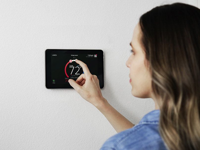A woman is adjusting the temperature on a thermostat.