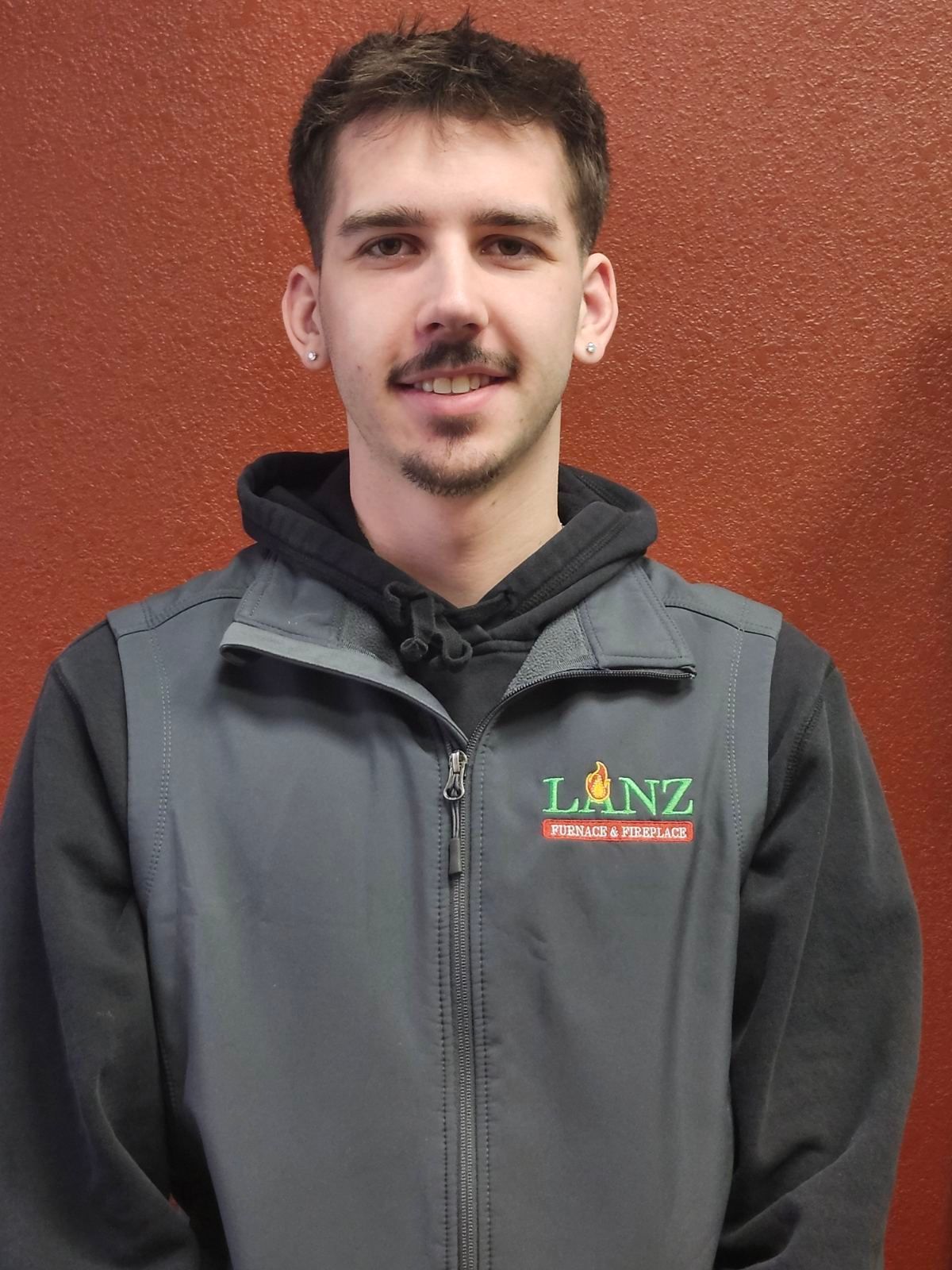 A young man with a mustache is wearing a jacket with the word lanz on it.