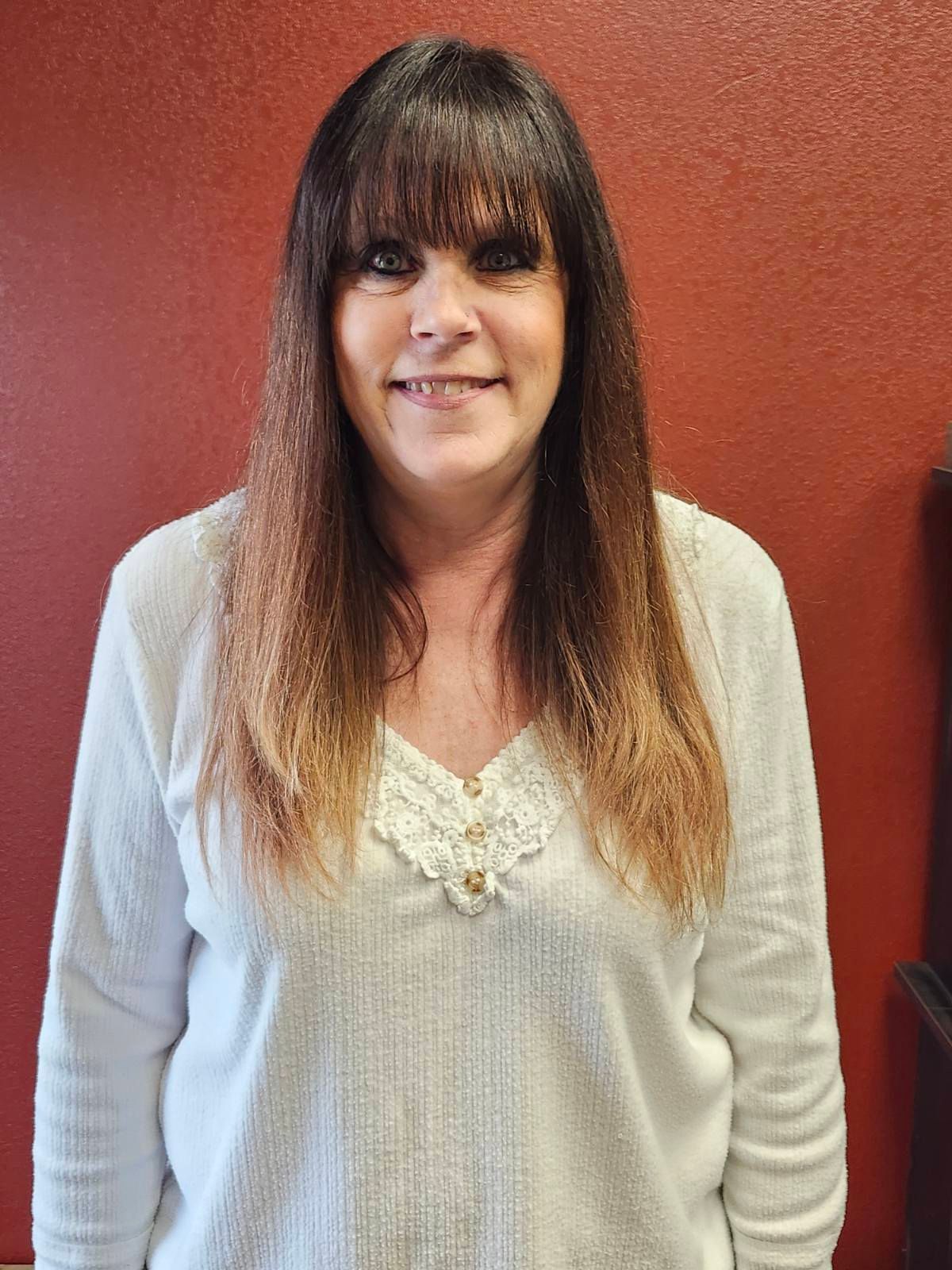 A woman in a white sweater is standing in front of a red wall.