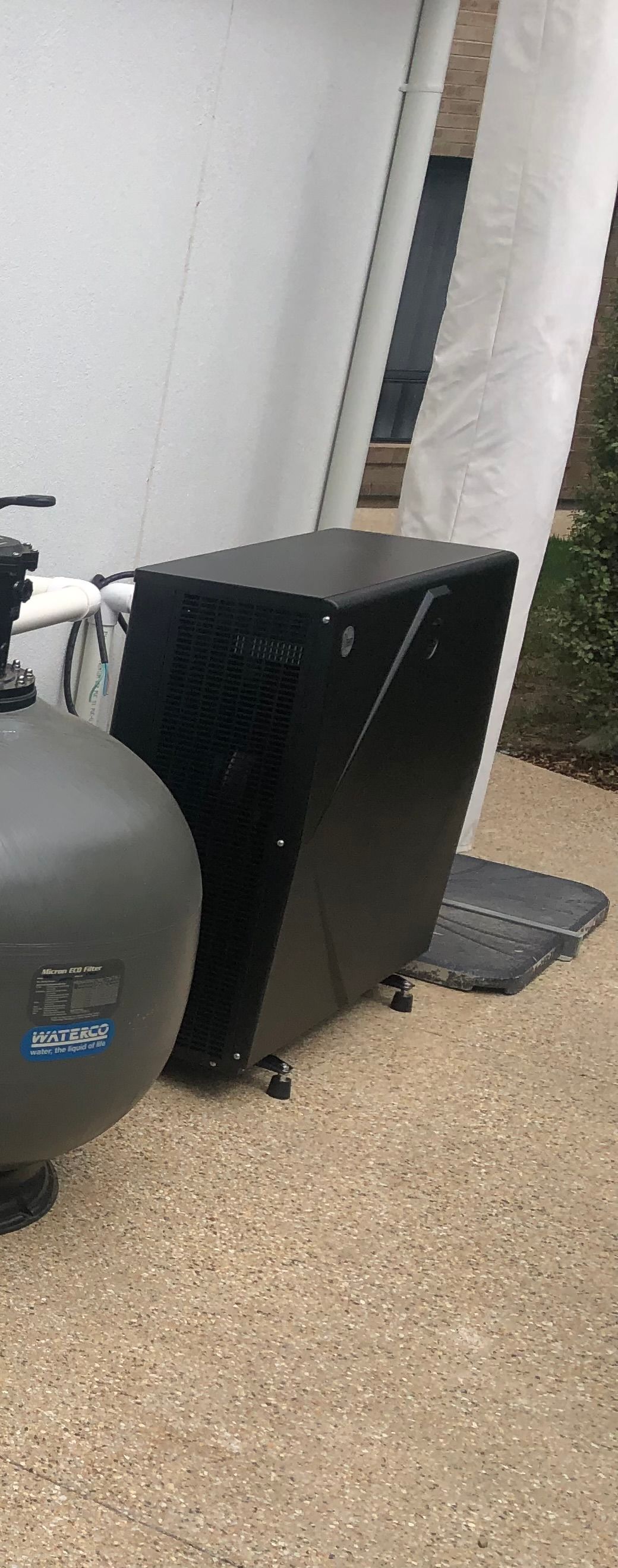 A Black pool heat pump is against a wall with a pool pump next to it — Mediterranean Custom Pools In Kialla, VIC