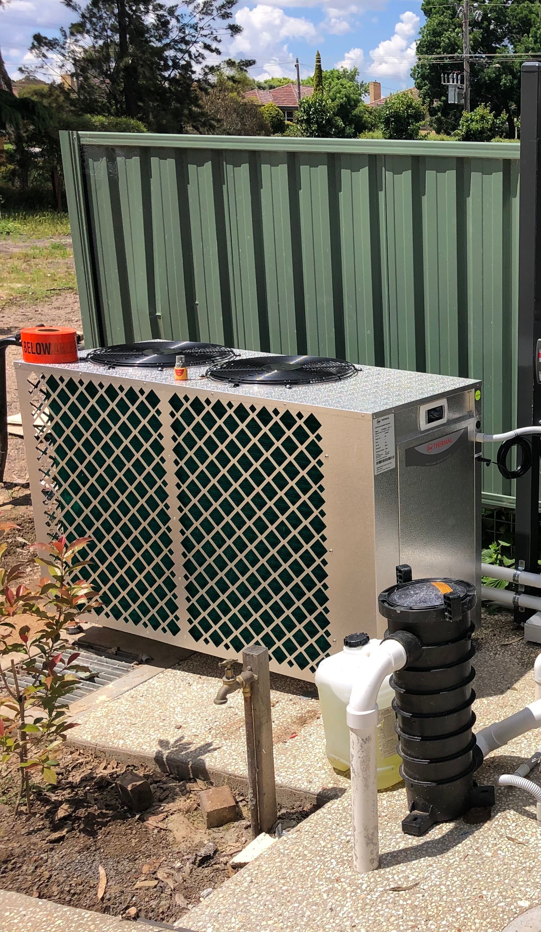 A large silver heat pump next to a green shed — Mediterranean Custom Pools In Kialla, VIC