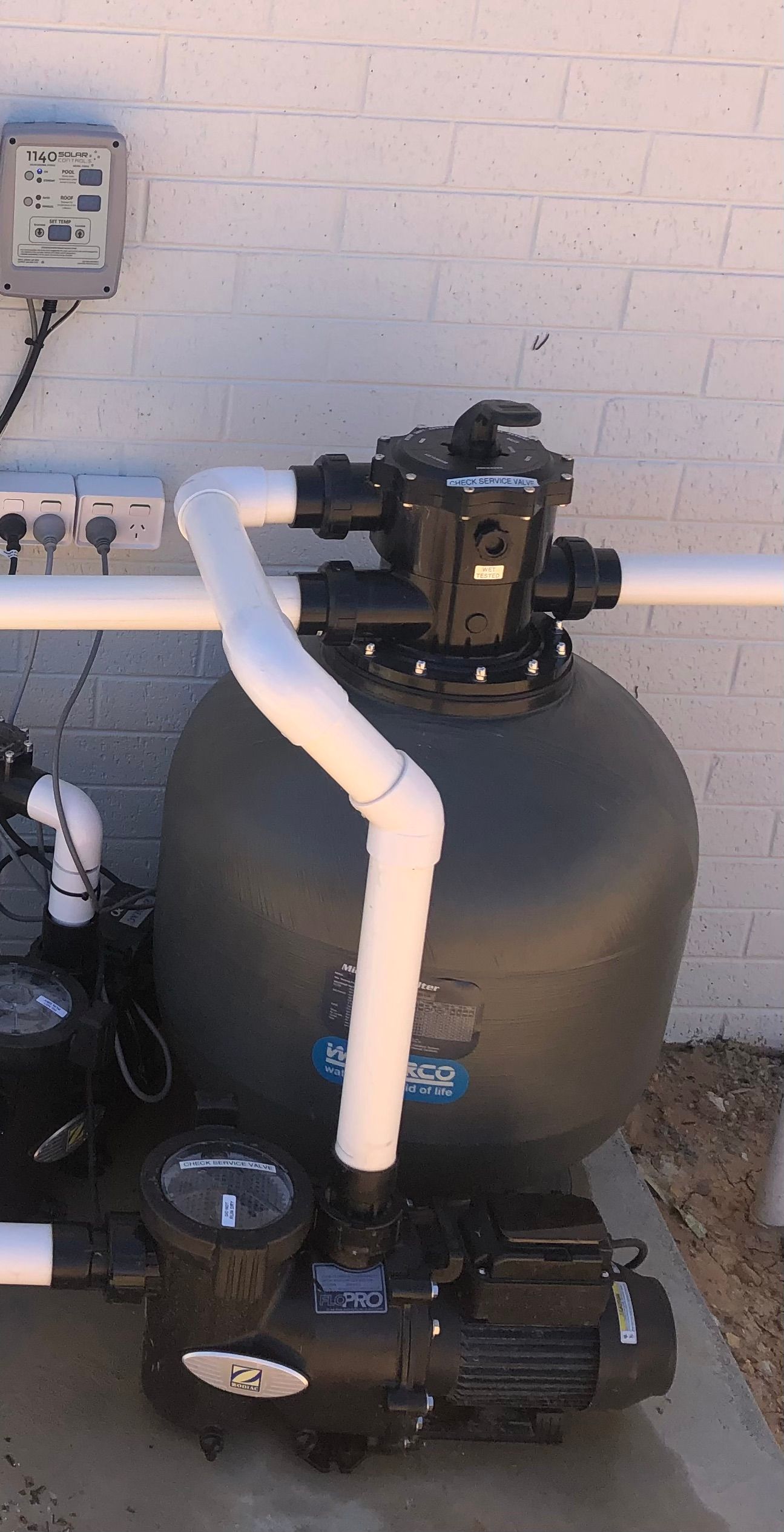 A black pool filter is sitting on the ground next to a brick wall — Mediterranean Custom Pools In Kialla, VIC