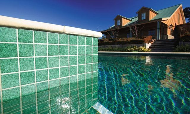 A Swimming Pool With Green Tiles And A House In The Background — Mediterranean Custom Pools In Kialla, VIC