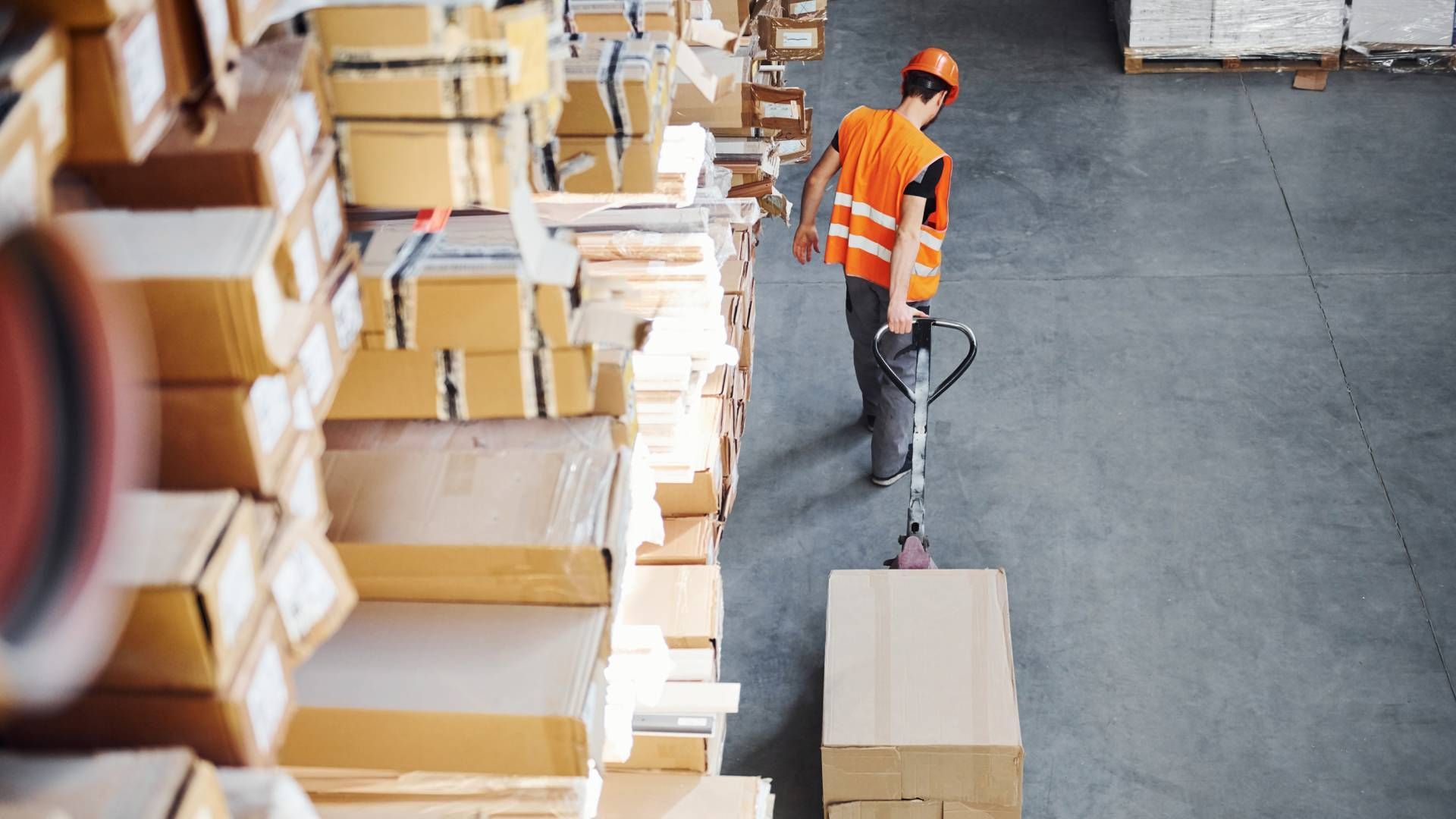 A distribution center employee pulling a crate on a cart near a large stack of crates at  C & S Tran