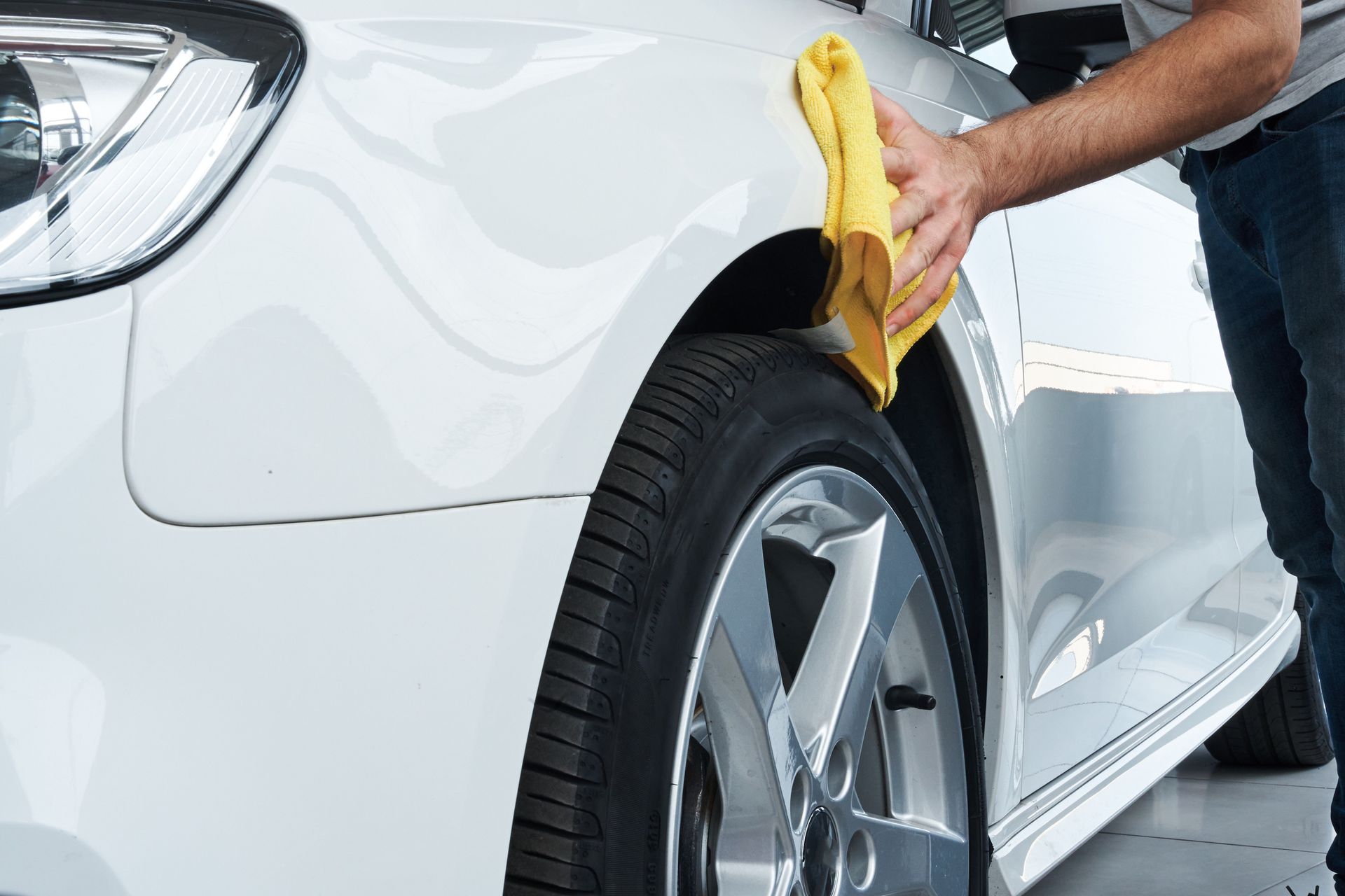 A man is cleaning a white car with a yellow cloth.