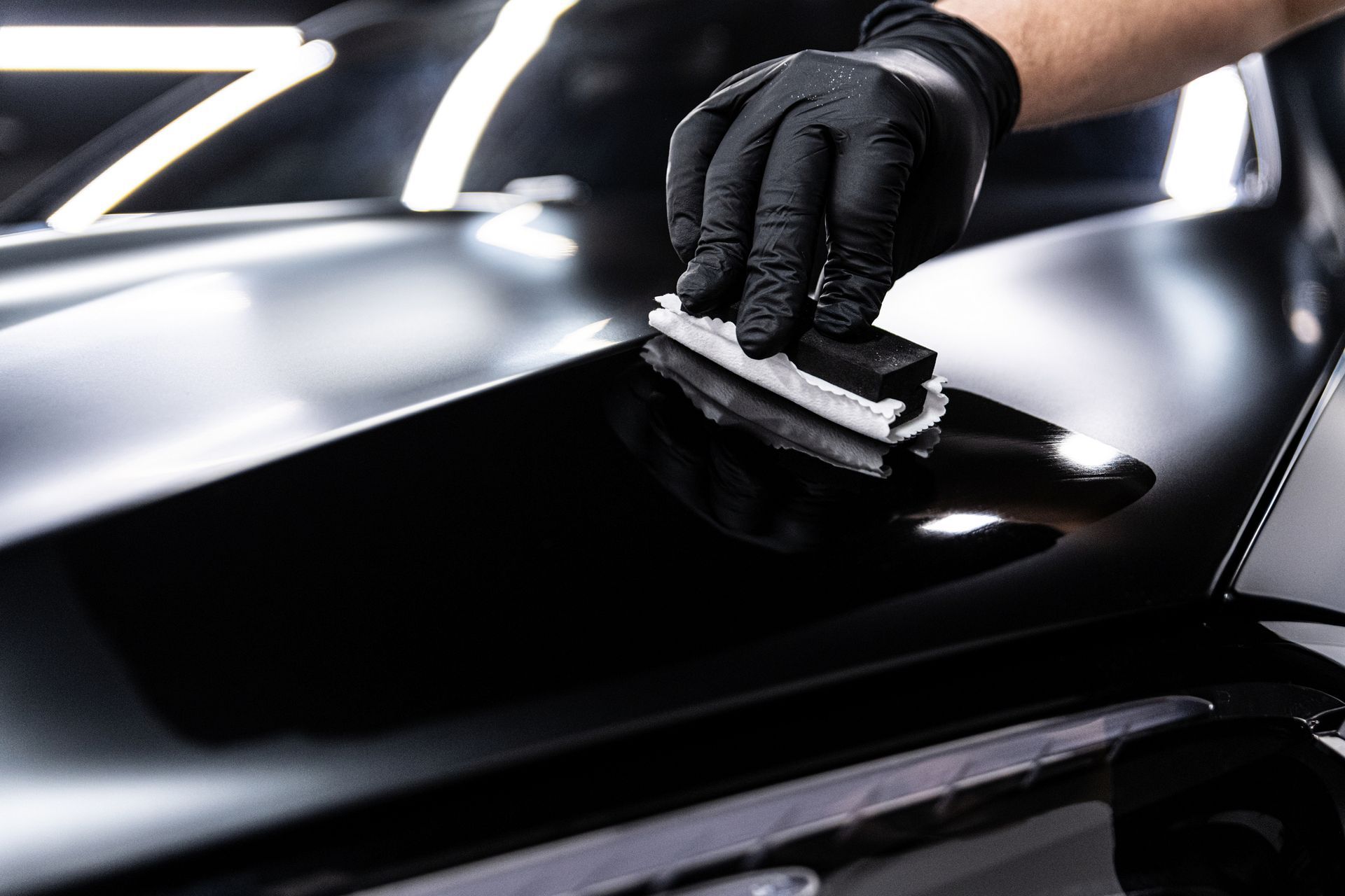 A person is polishing the hood of a car with a sponge. A person is polishing the hood of a car with a sponge.
