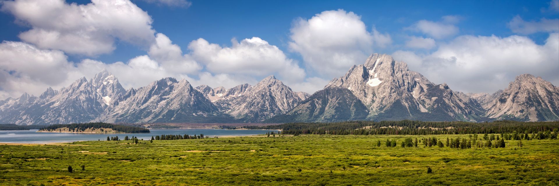 A mountain range with a lake in the foreground and a grassy field in the foreground.
