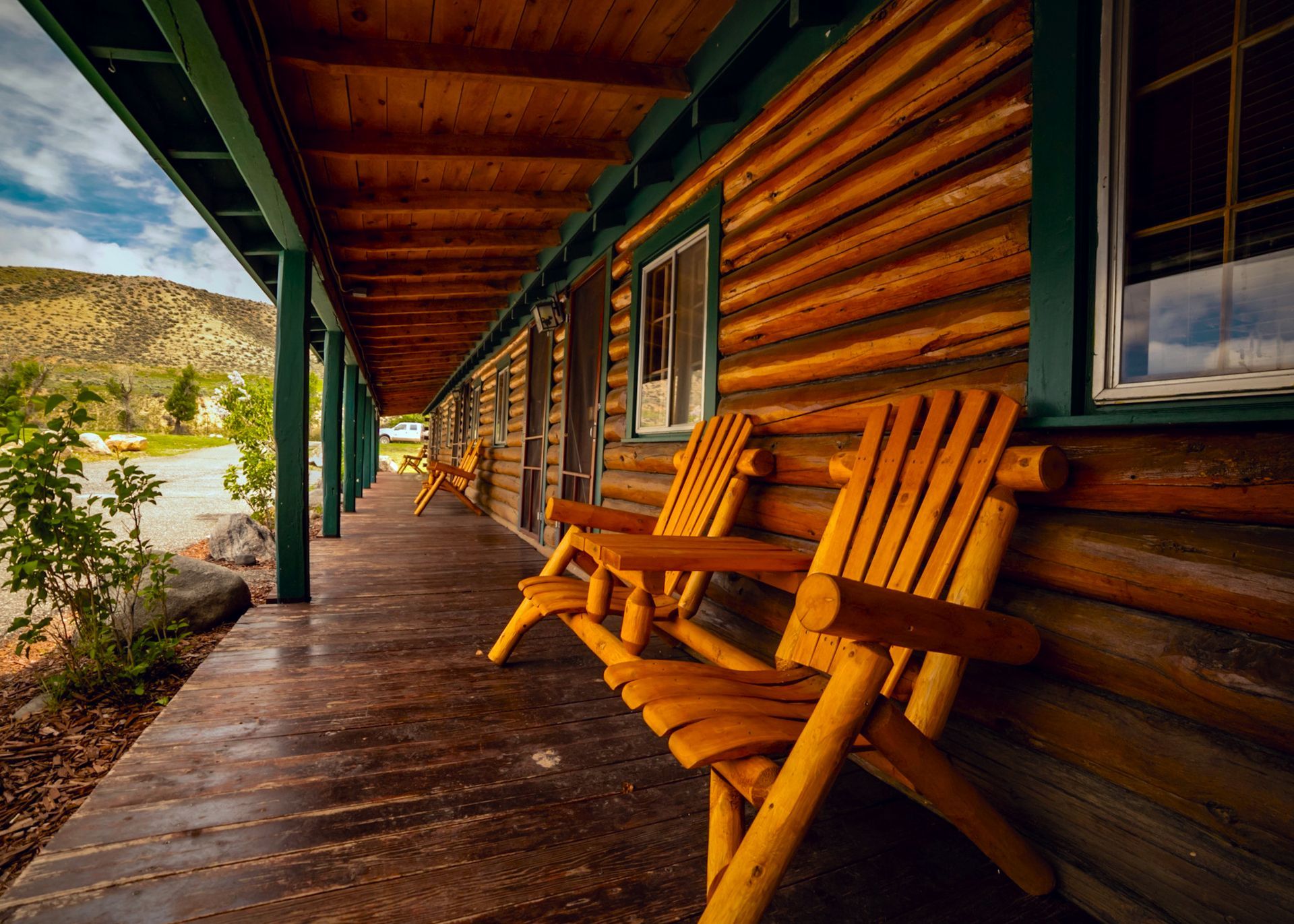 Two wooden chairs are sitting on the porch of a log cabin.