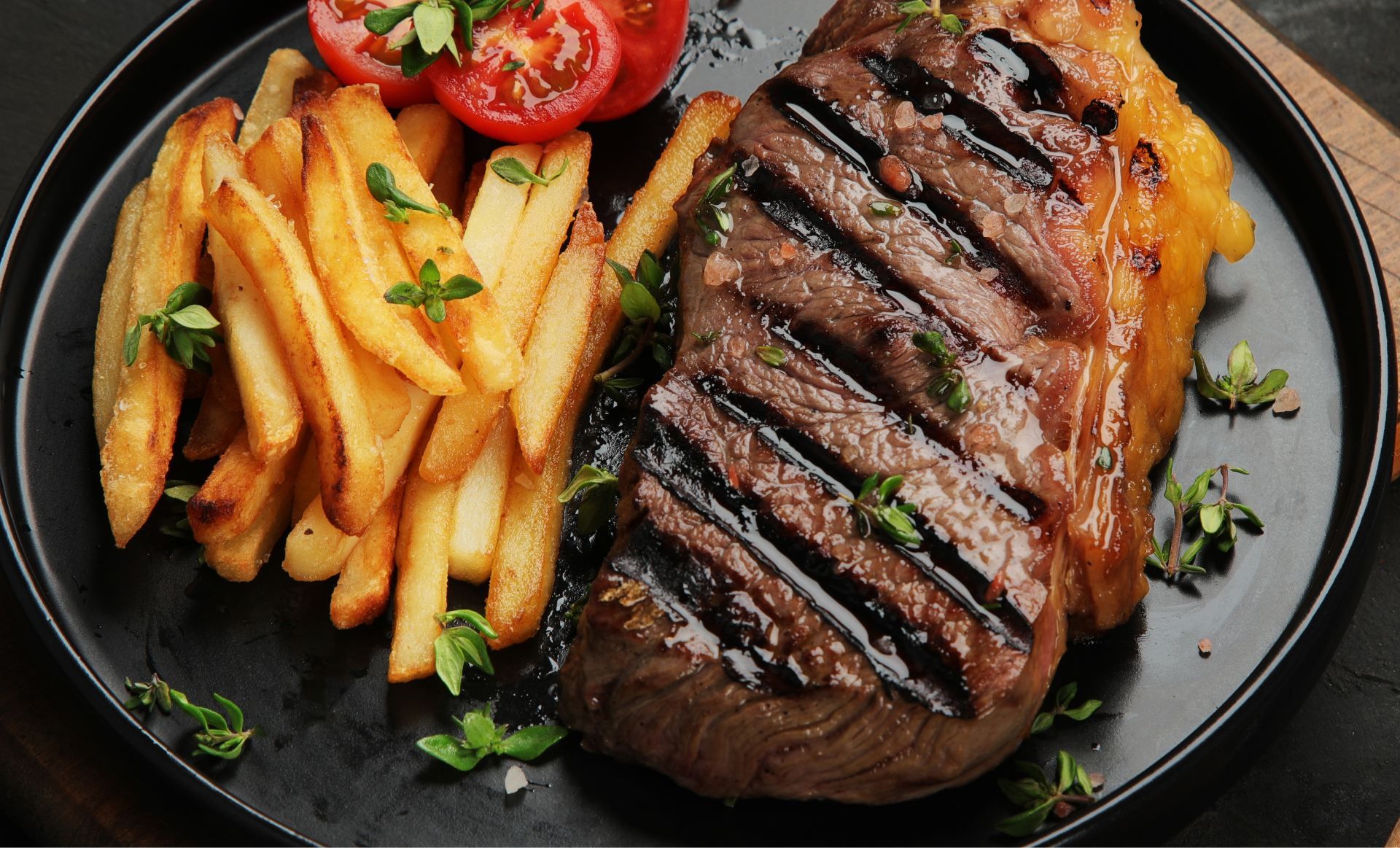 A grilled steak and french fries on a black plate.