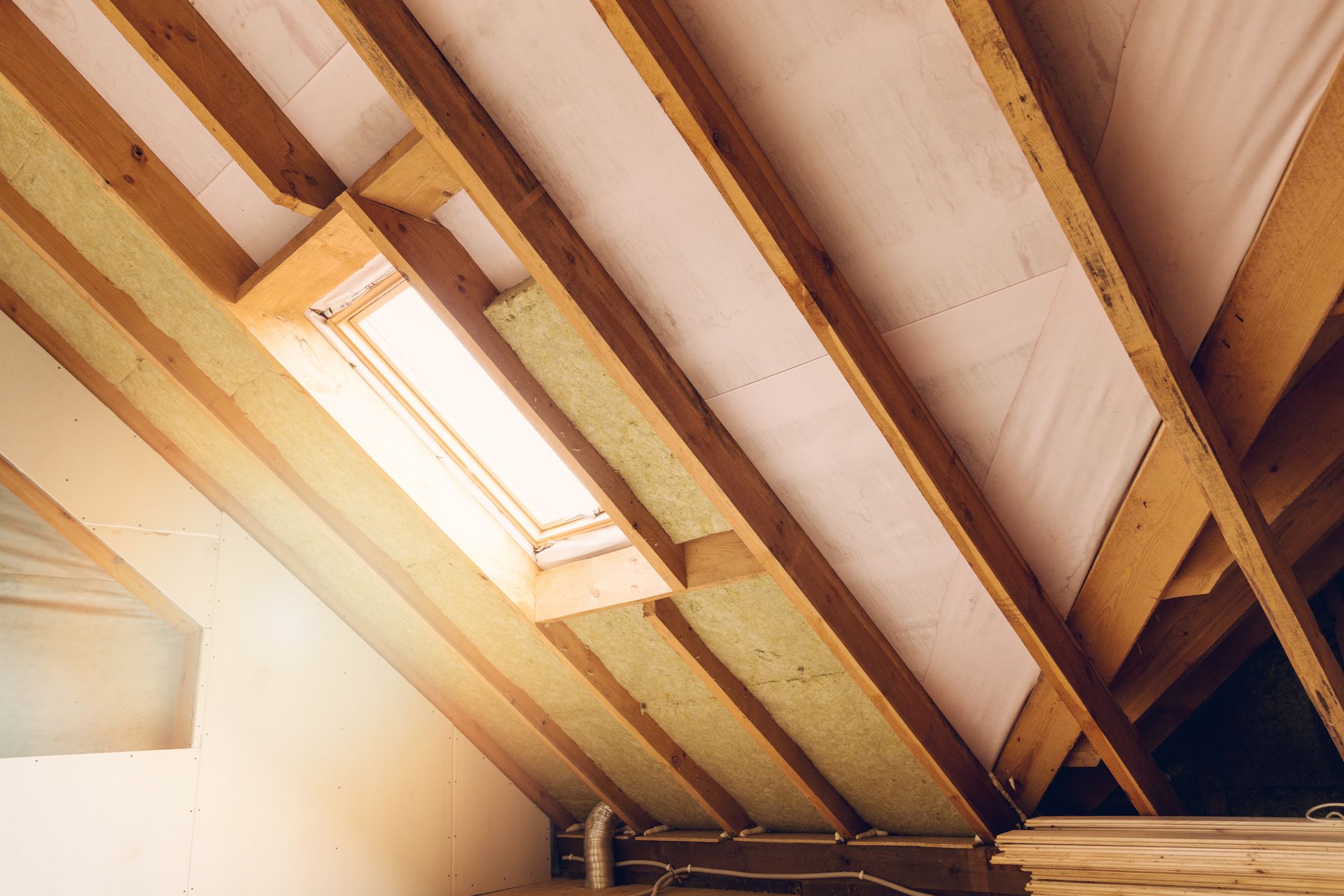 Sunlit attic ceiling with exposed wooden beams and a skylight window