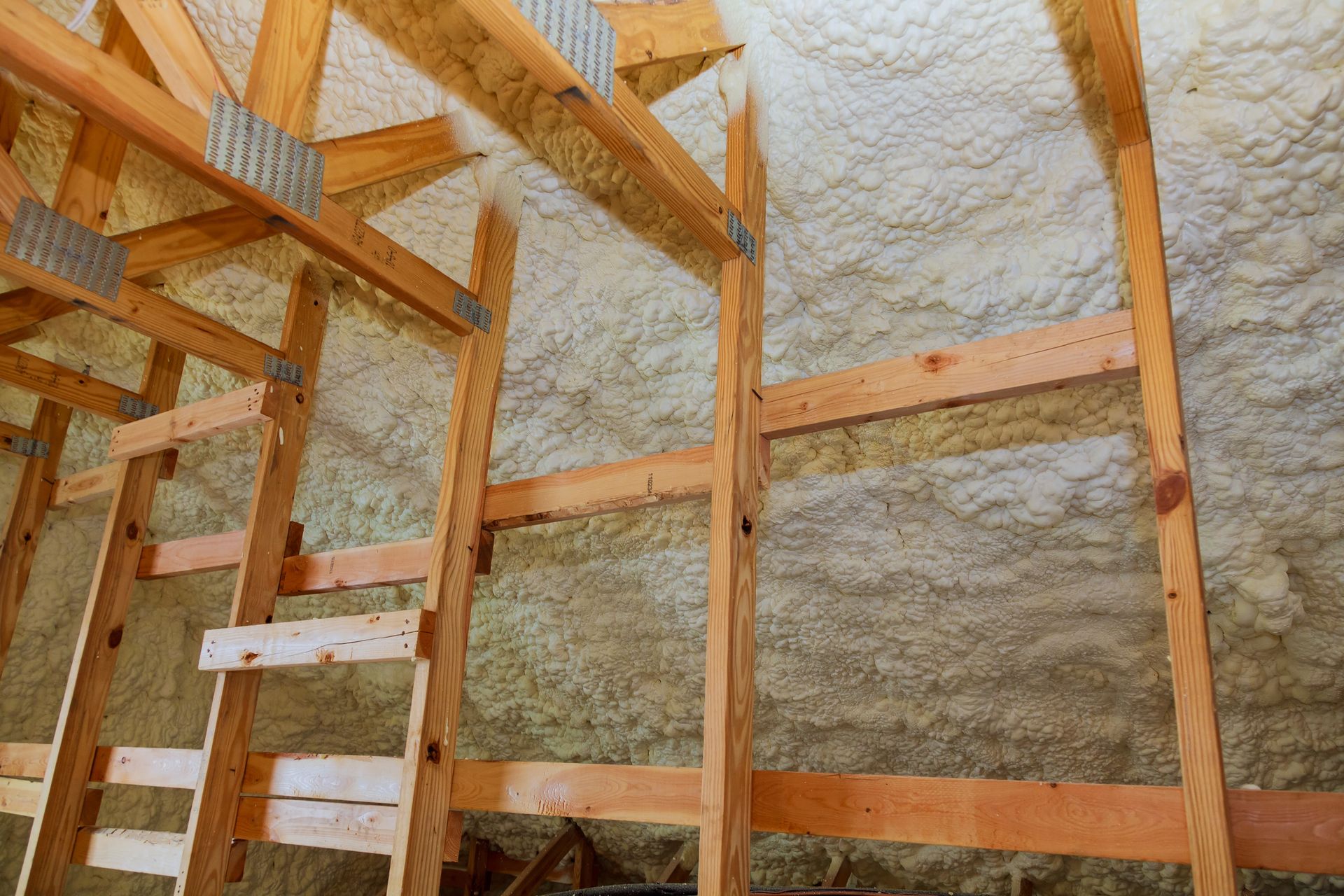Wooden framing inside an attic with white spray foam insulation on the walls and ceiling