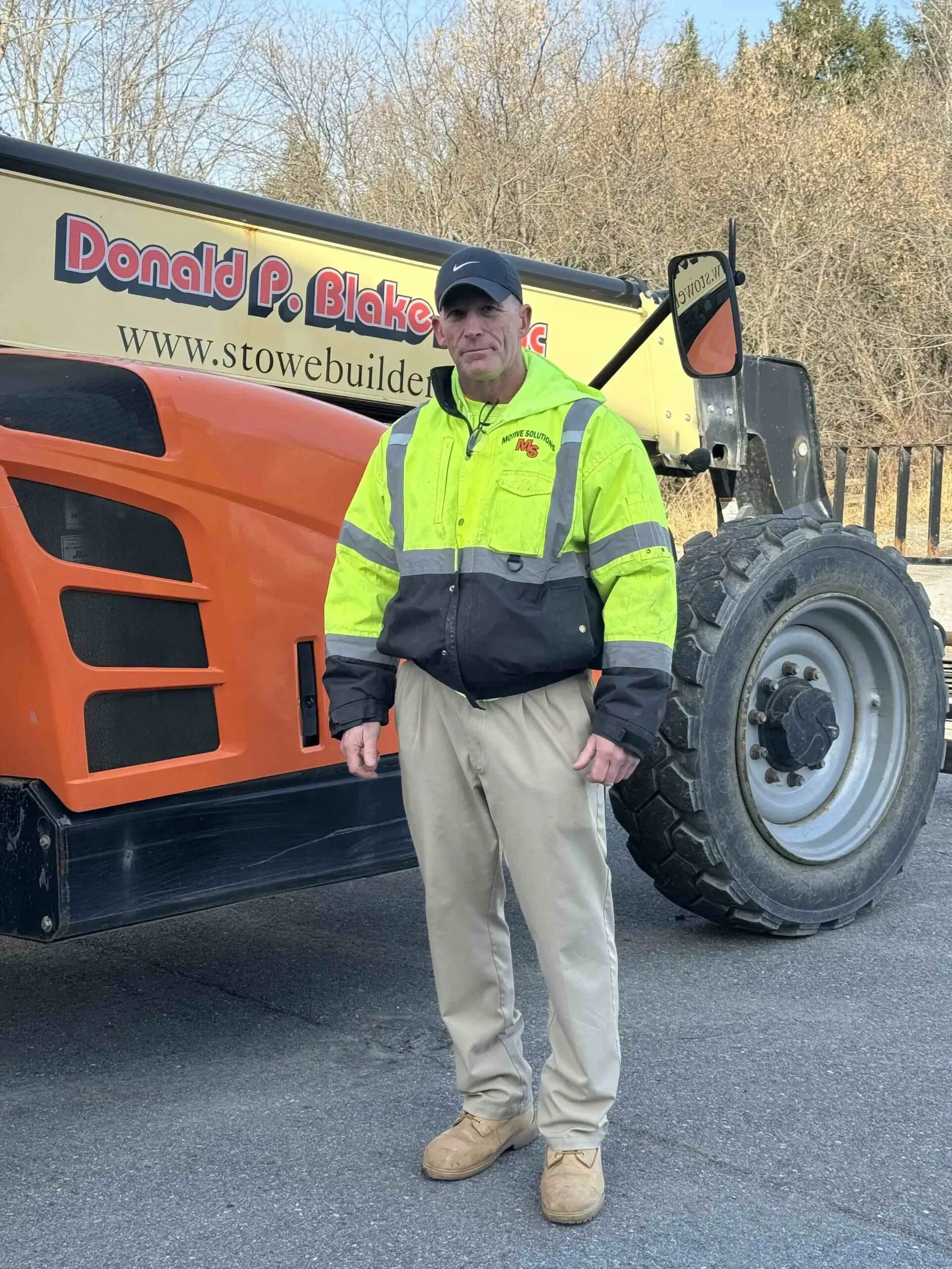 Paul Soracco of Motive Solutions LLC in a high-visibility jacket stands in front of a construction telehandler outdoors.