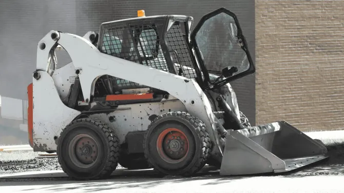 A white skid-steer loader with a front bucket parked on a paved surface.
