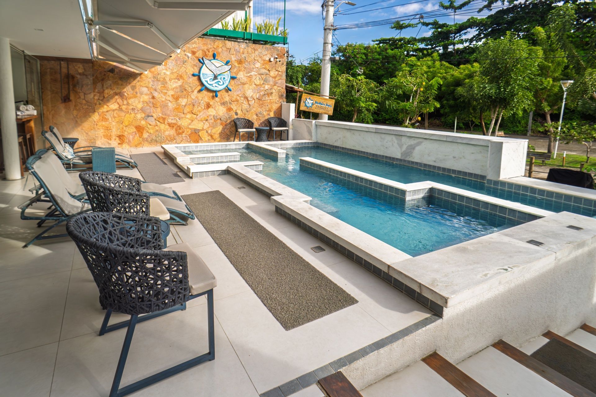 Pátio moderno com piscina retangular, espreguiçadeiras e parede de pedra com detalhes em cobertura.