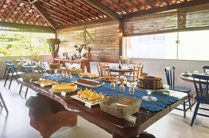 Mesa de bufê com sobremesas e bebidas sob um pavilhão de madeira, preparada para uma refeição ao ar livre.