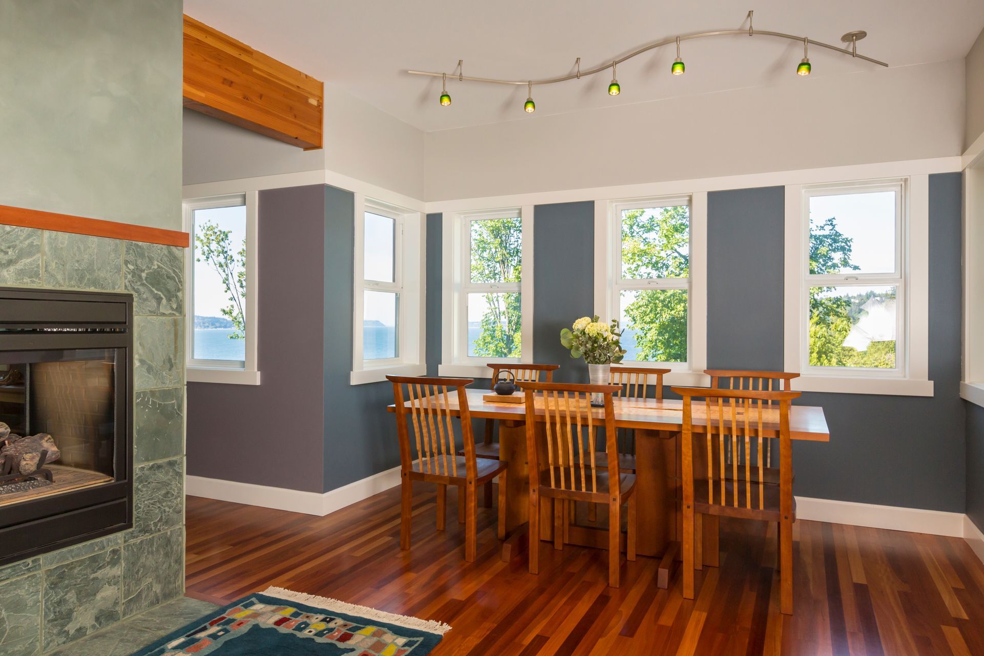 Dining room with a wooden table, chairs, large windows, hardwood floors, and a fireplace.
