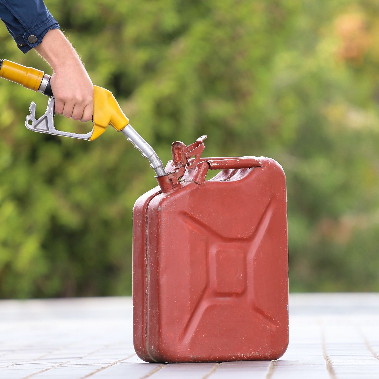 A person is pumping gas into a red gas can.