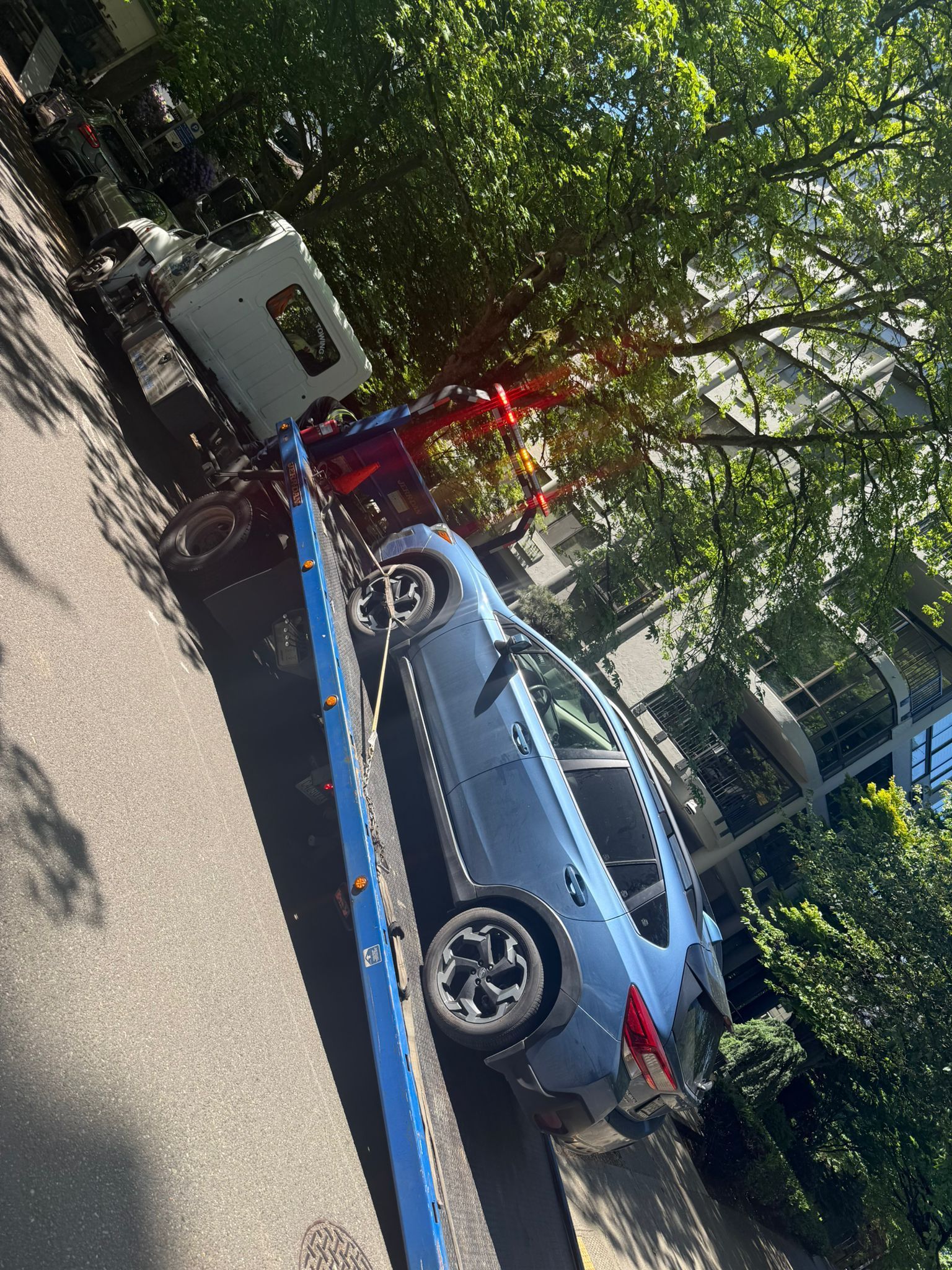 A blue car is being towed down a street by a tow truck.
