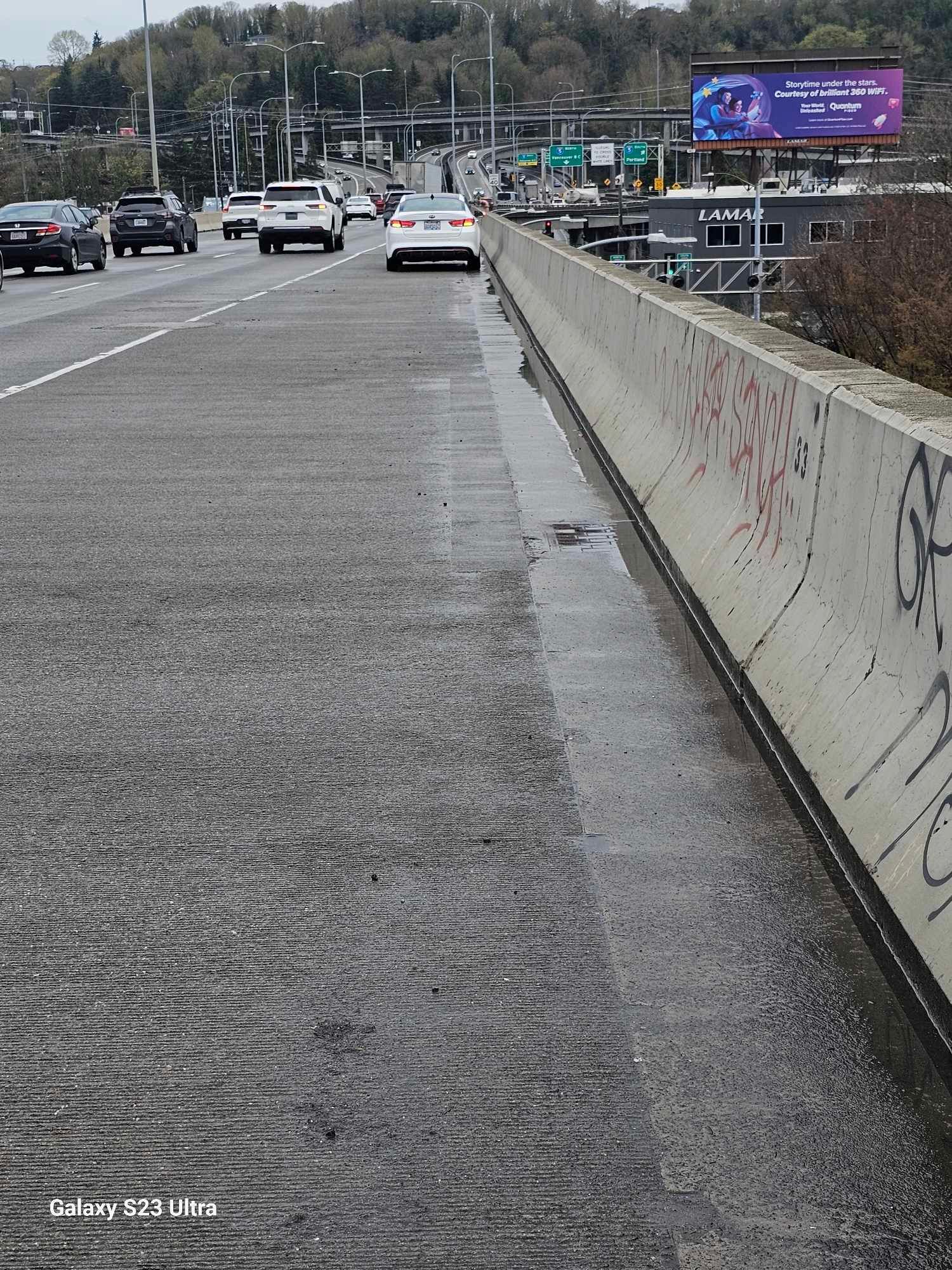 Cars are driving down a highway next to a concrete wall with graffiti on it