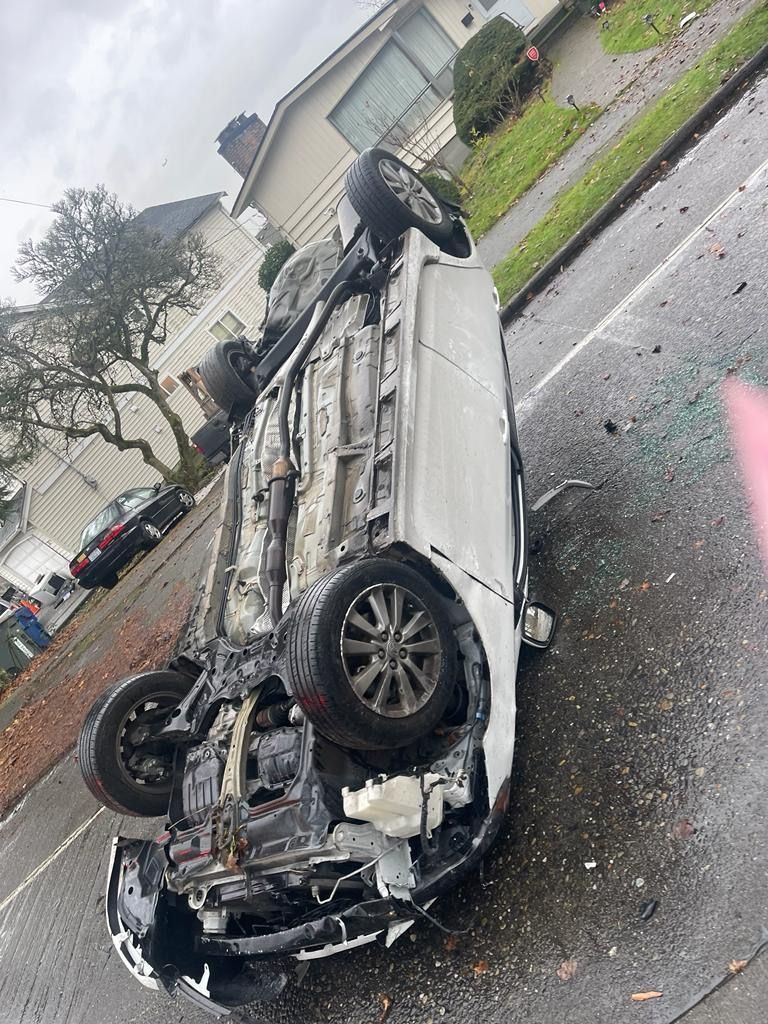 A white car is upside down on the side of the road.