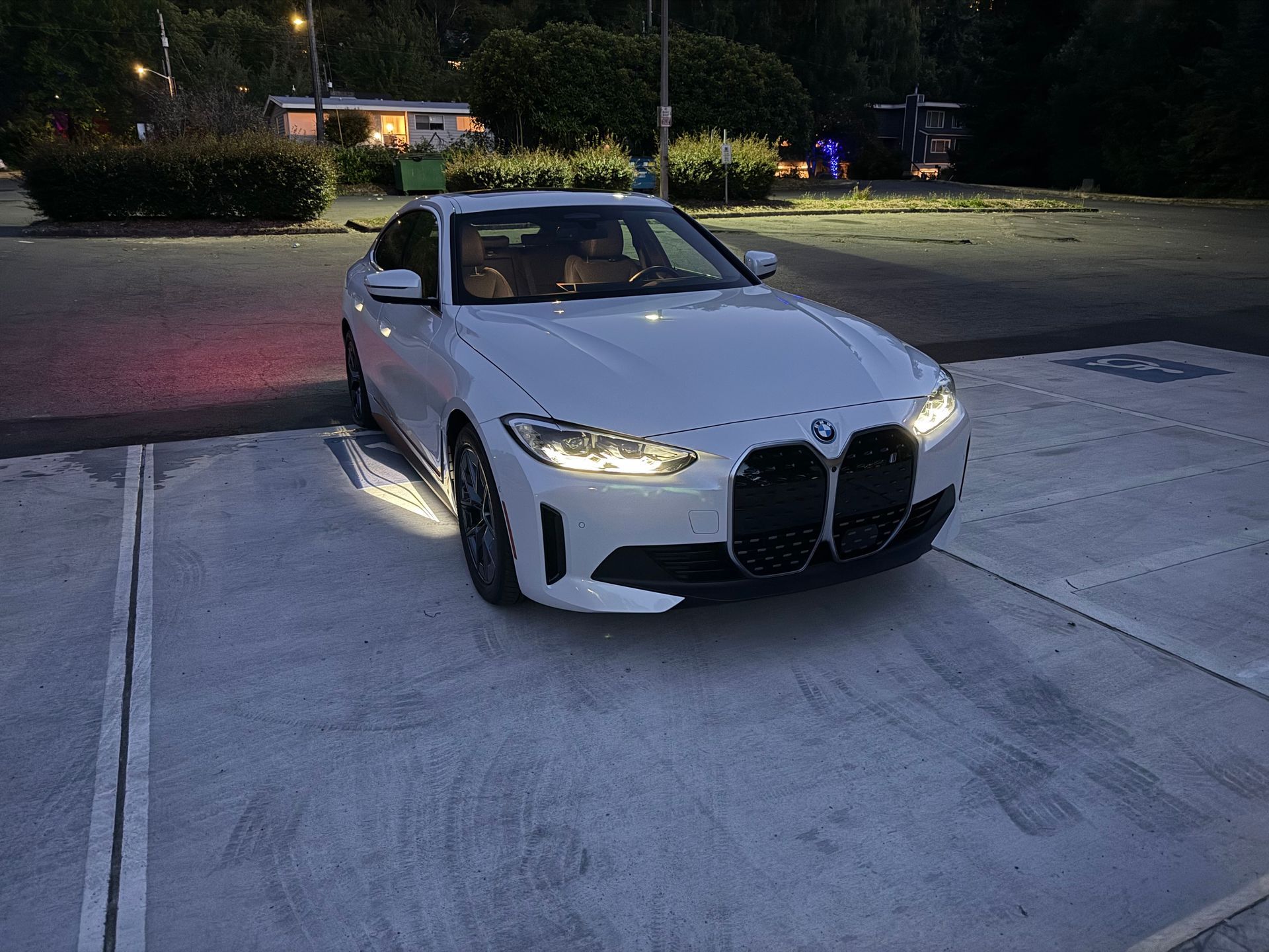 A white bmw is parked in a parking lot at night.
