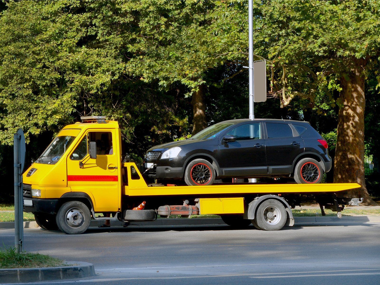 A yellow tow truck is carrying a black car on its flatbed.