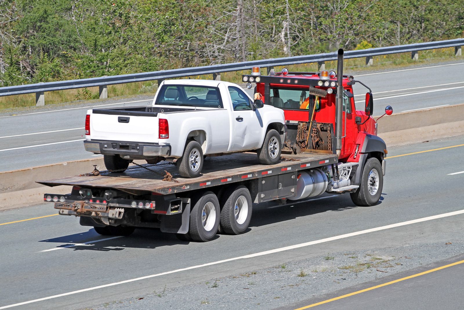 White pickup truck on a red flatbed tow truck traveling on a highway.