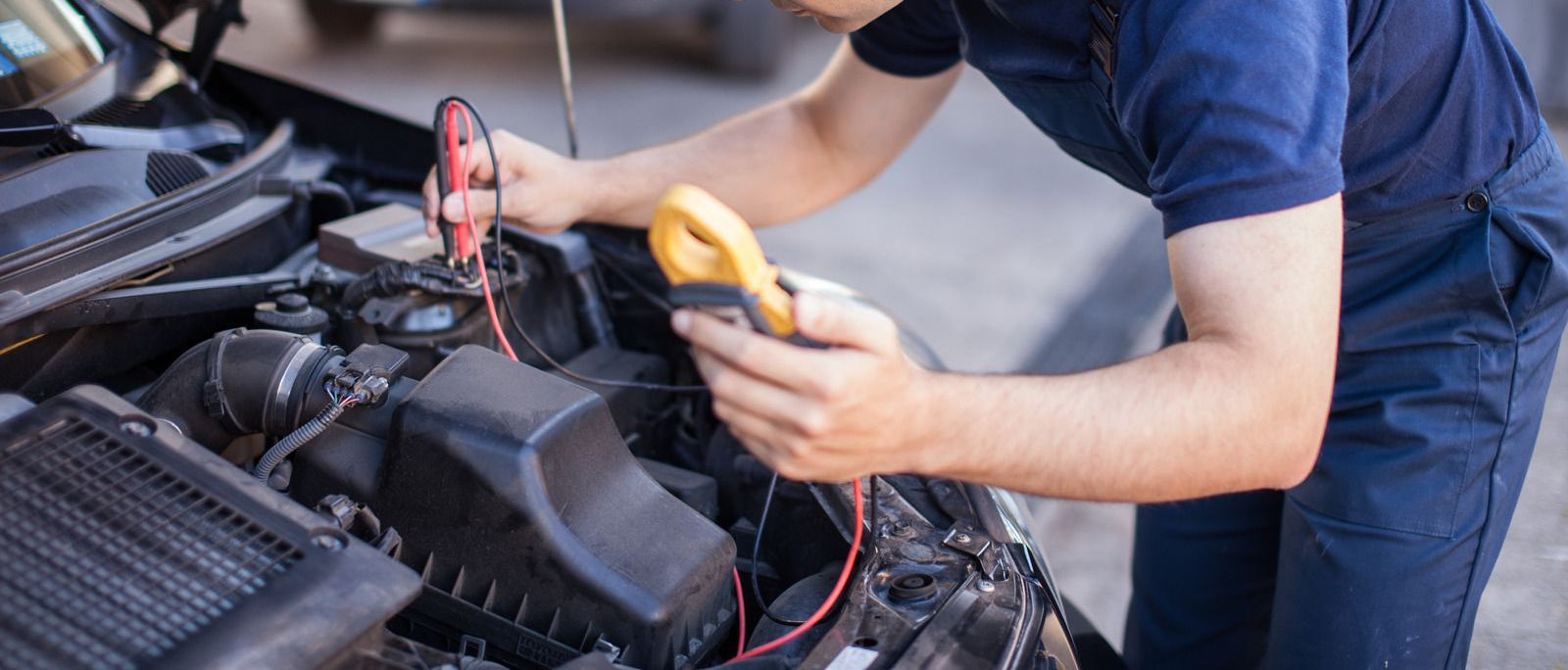 A man is working on a car with a multimeter.