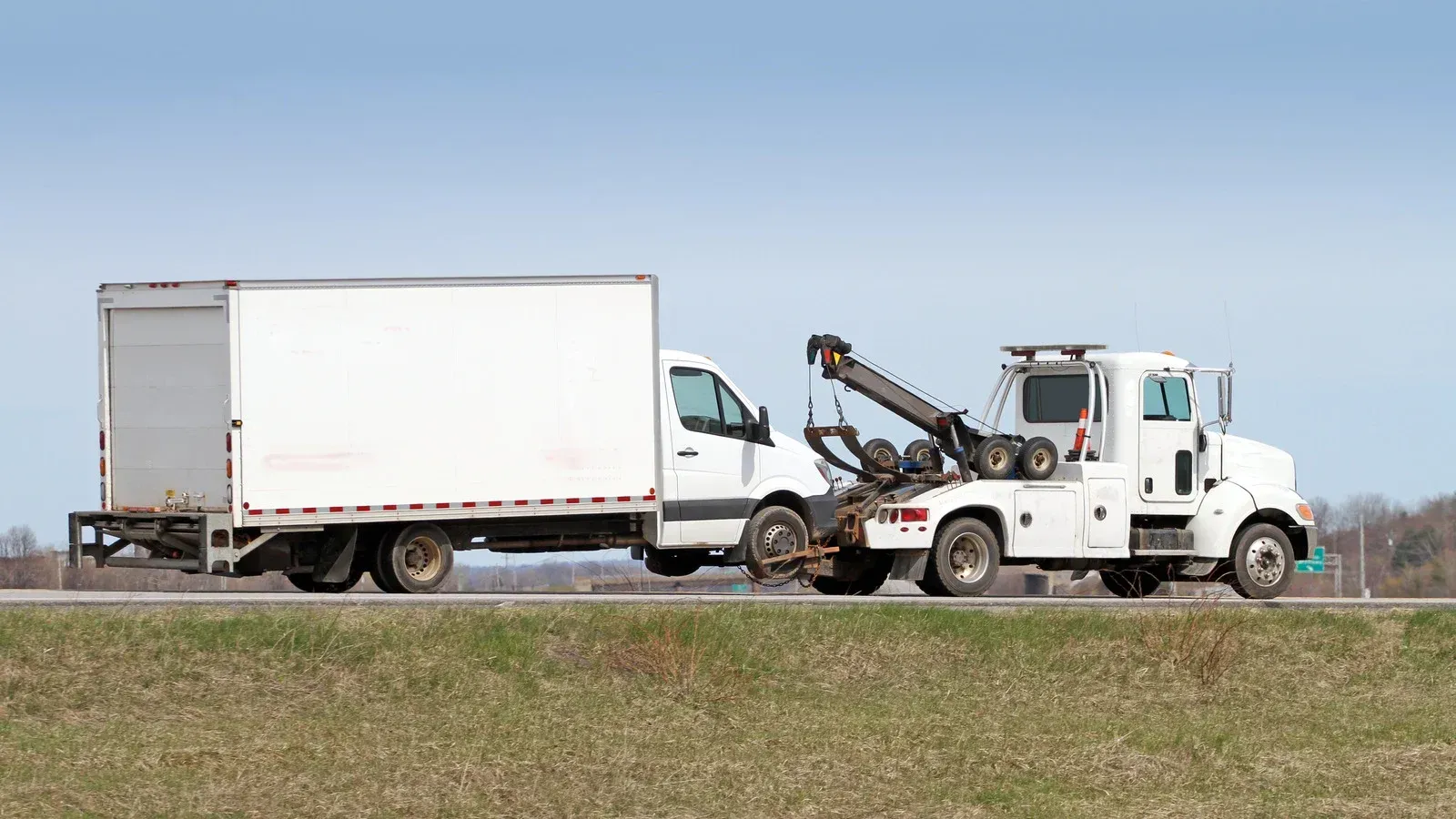 A white tow truck is towing a white truck down the road.