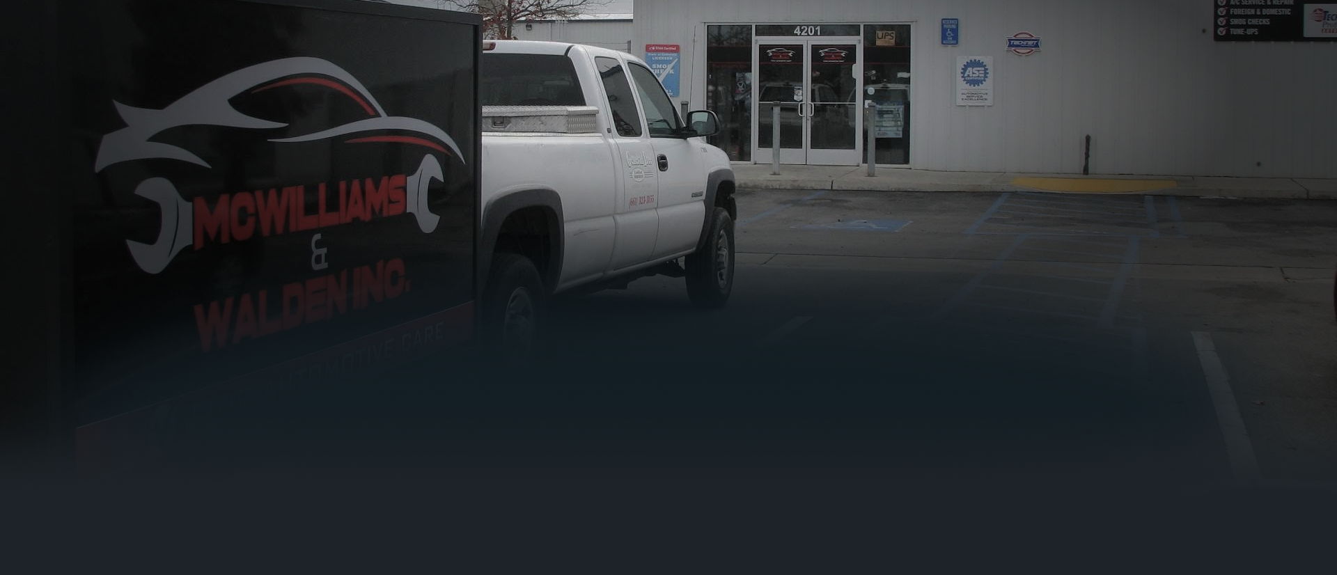 A white pickup truck parked in front of an auto shop with the business logo on the side.