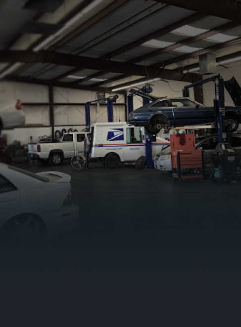 Inside a garage, USPS truck and other vehicles, some on lifts, are being worked on.