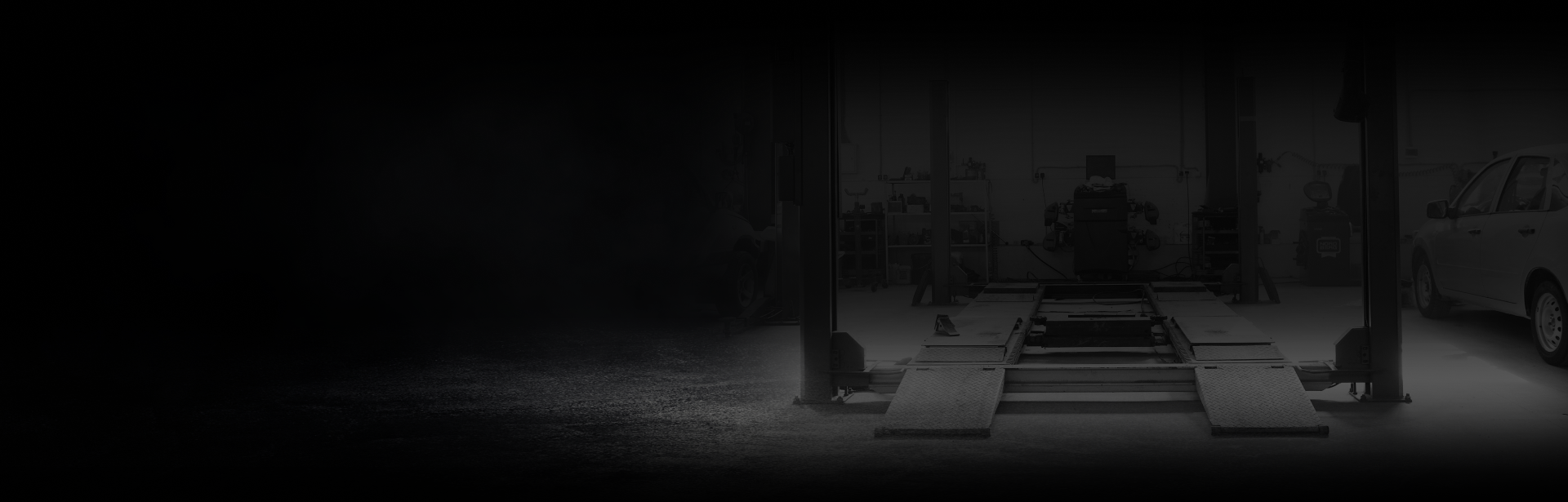 A dimly lit auto shop interior with a person working near a car lift.